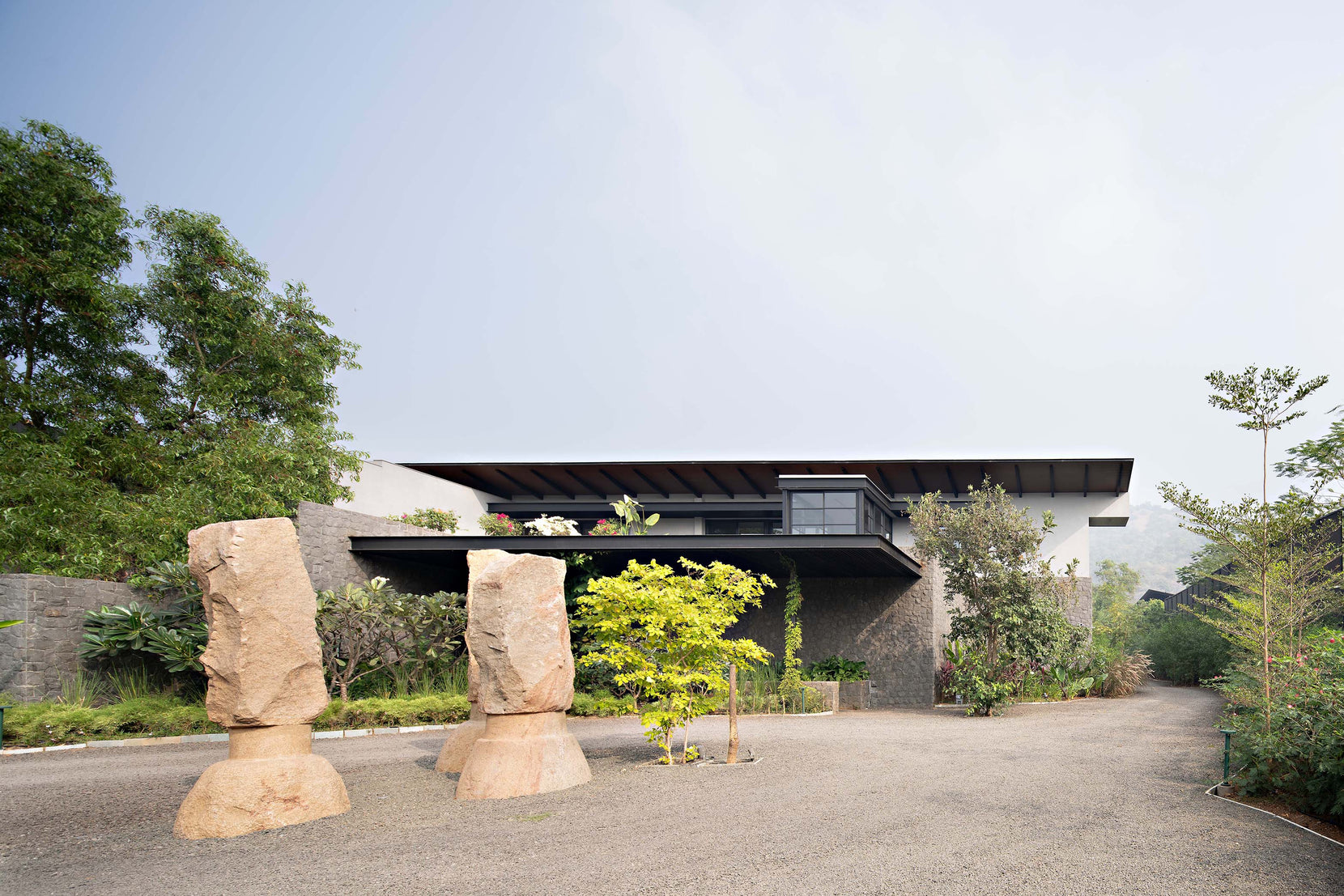 Two carved stone monoliths on the gravel forecourt before the low cantilevered roof
