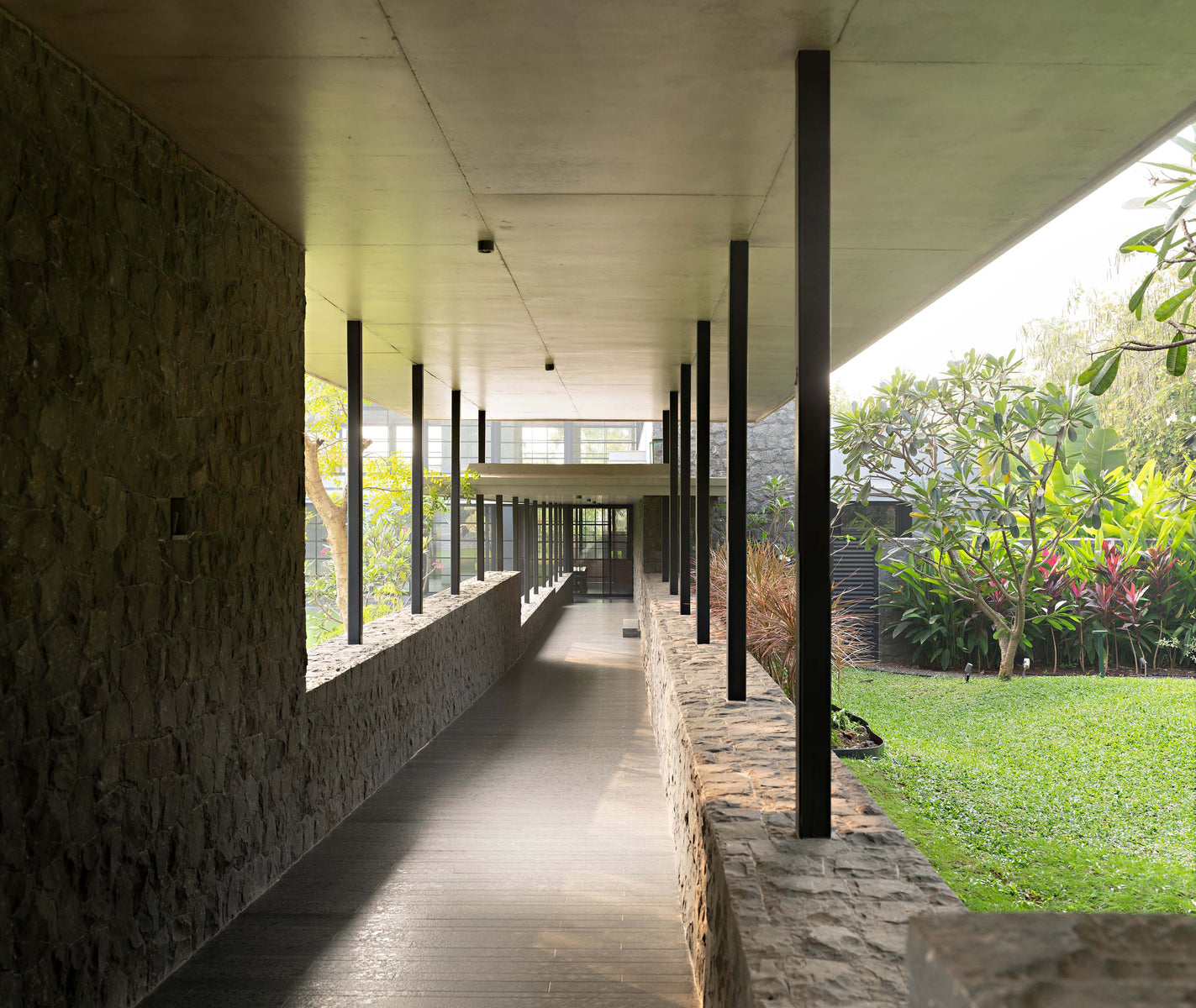 Colonnaded passage between rough stone walls, planting and lawn along one side