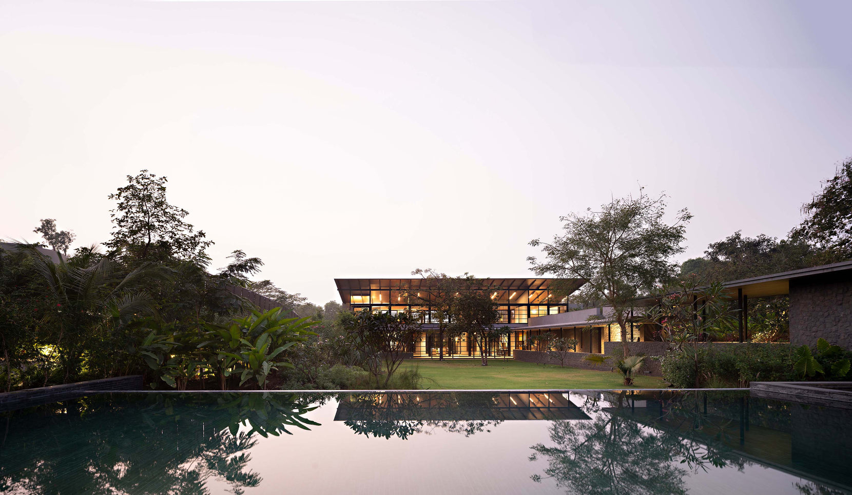 Alibaug Commune mirrored in the still pool at dusk, its long roof set among trees