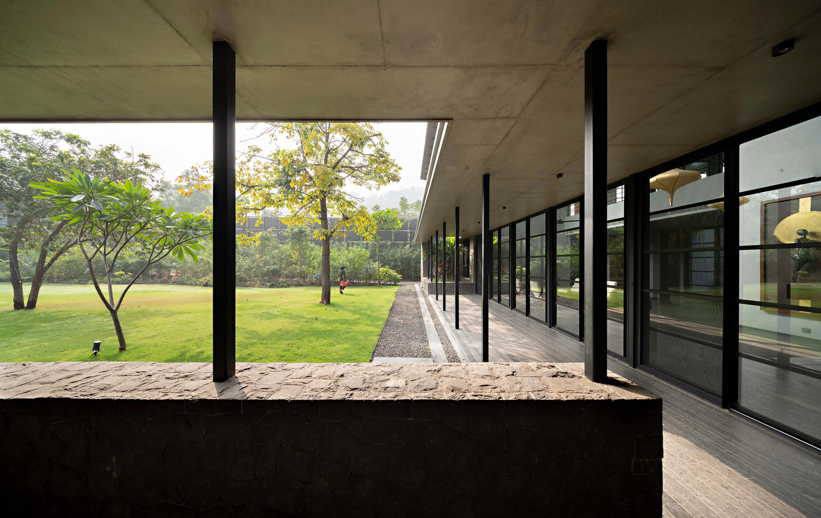 Sheltered walk beside glazed rooms, a low stone wall dividing the decking from the lawn
