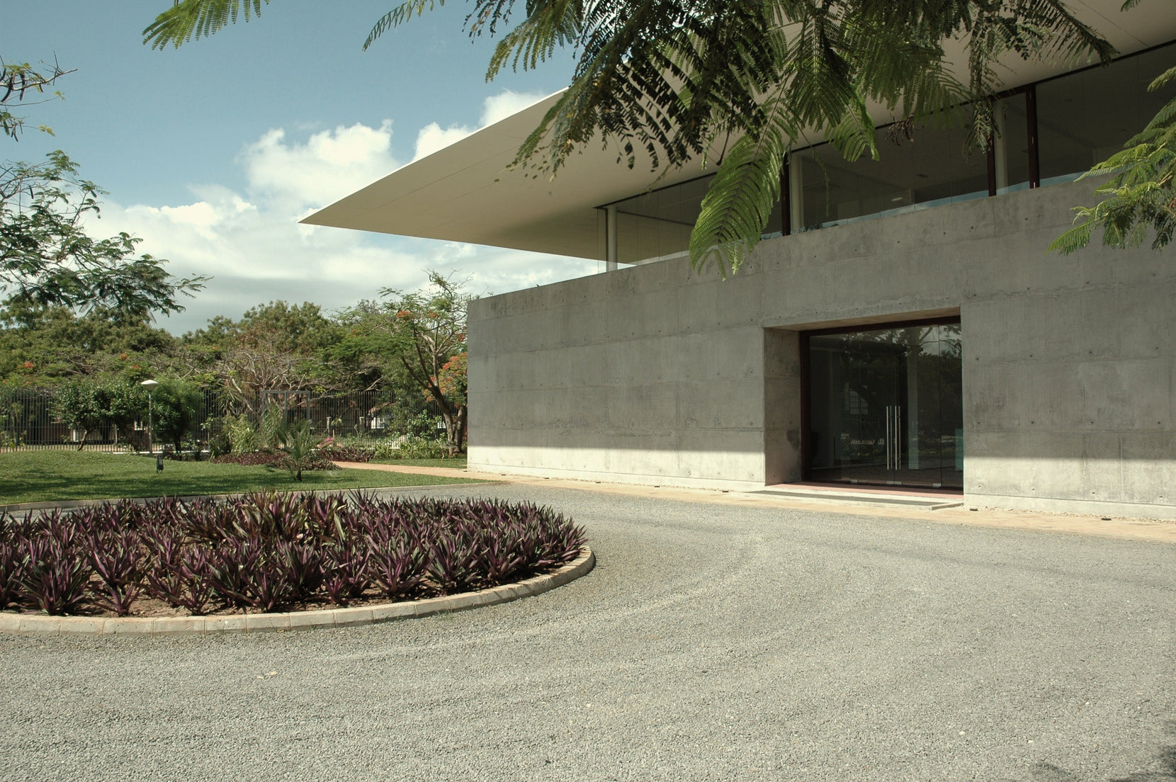 Gravel drive curving past the board-marked concrete wall to the glazed entrance