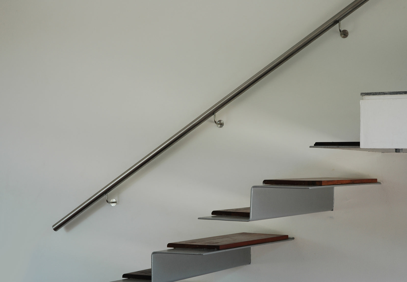 Cantilevered timber treads and a slim steel handrail set against a plain white wall