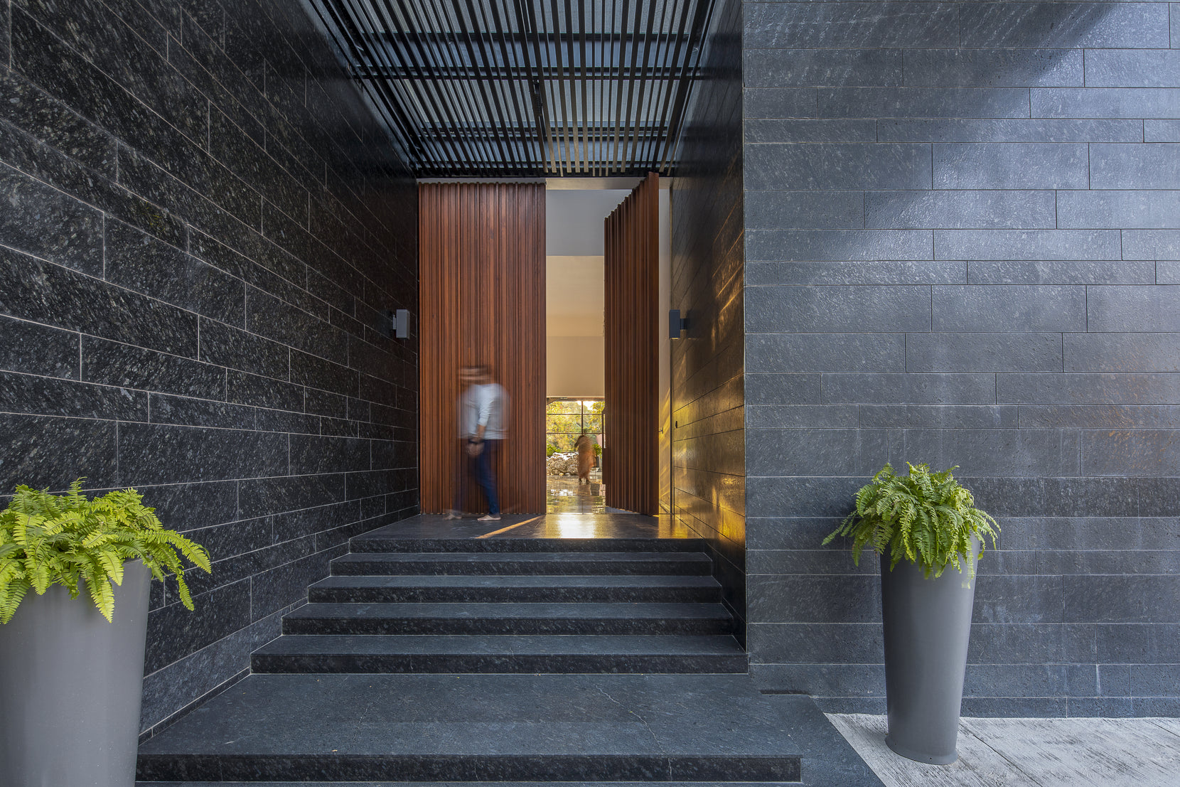 Granite-walled entrance steps rising to a timber screen door, ferns in tall planters either side