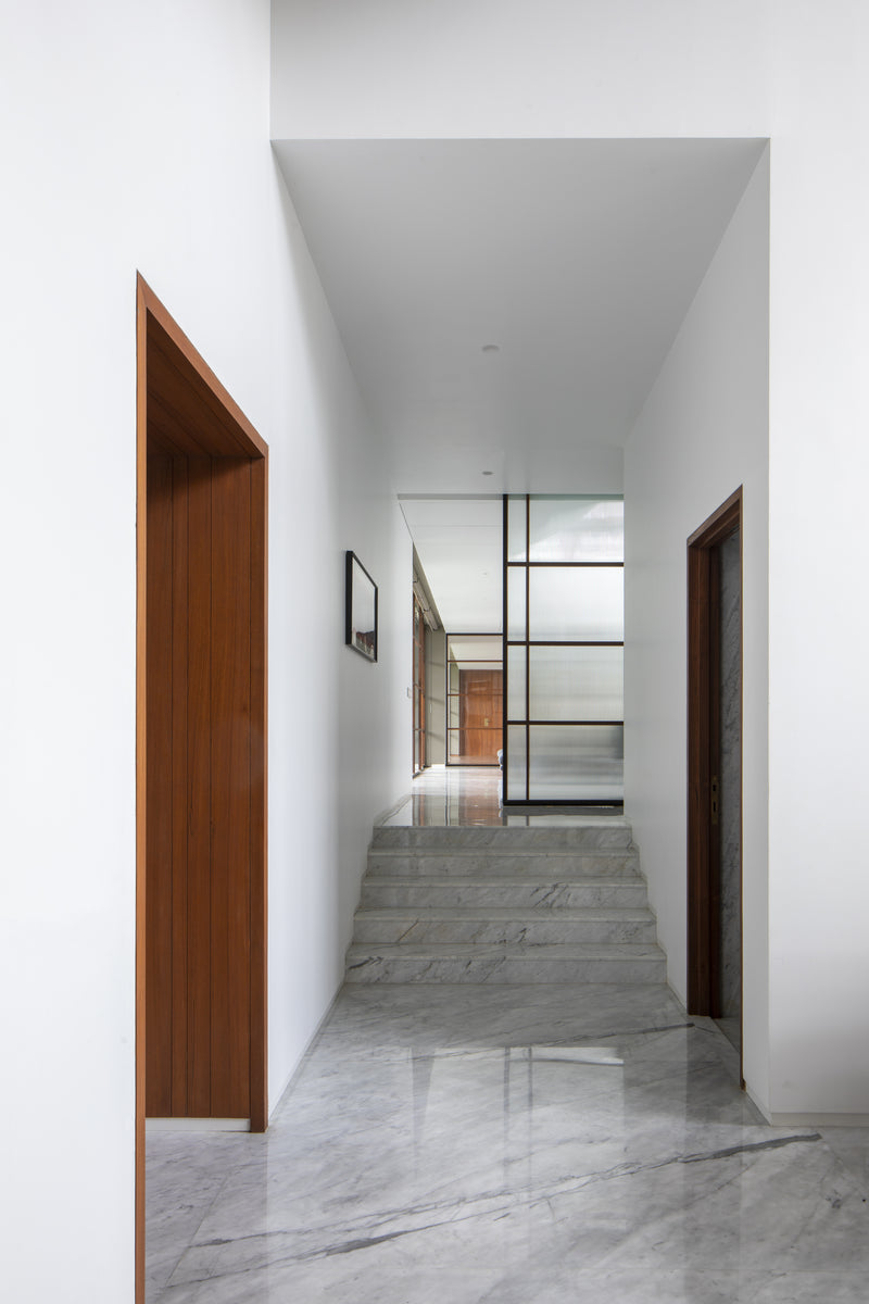 White corridor with marble steps and a teak-framed doorway leading through the house