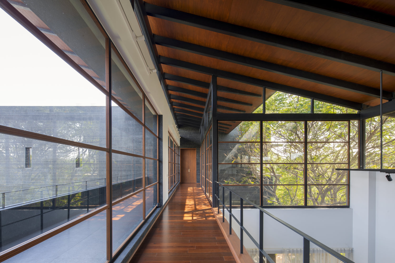 Upper gallery running under exposed timber rafters, glazed on both sides above the garden