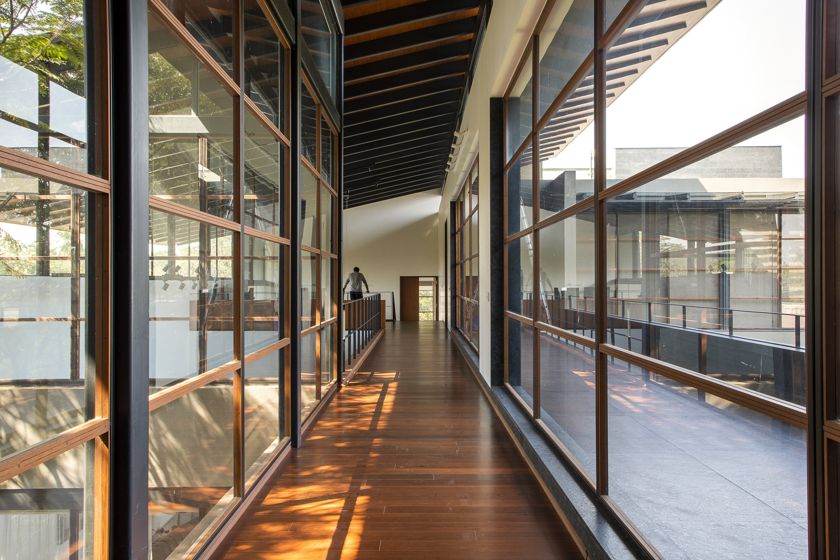 Figure at the end of the glazed first-floor gallery, light falling across the timber boards