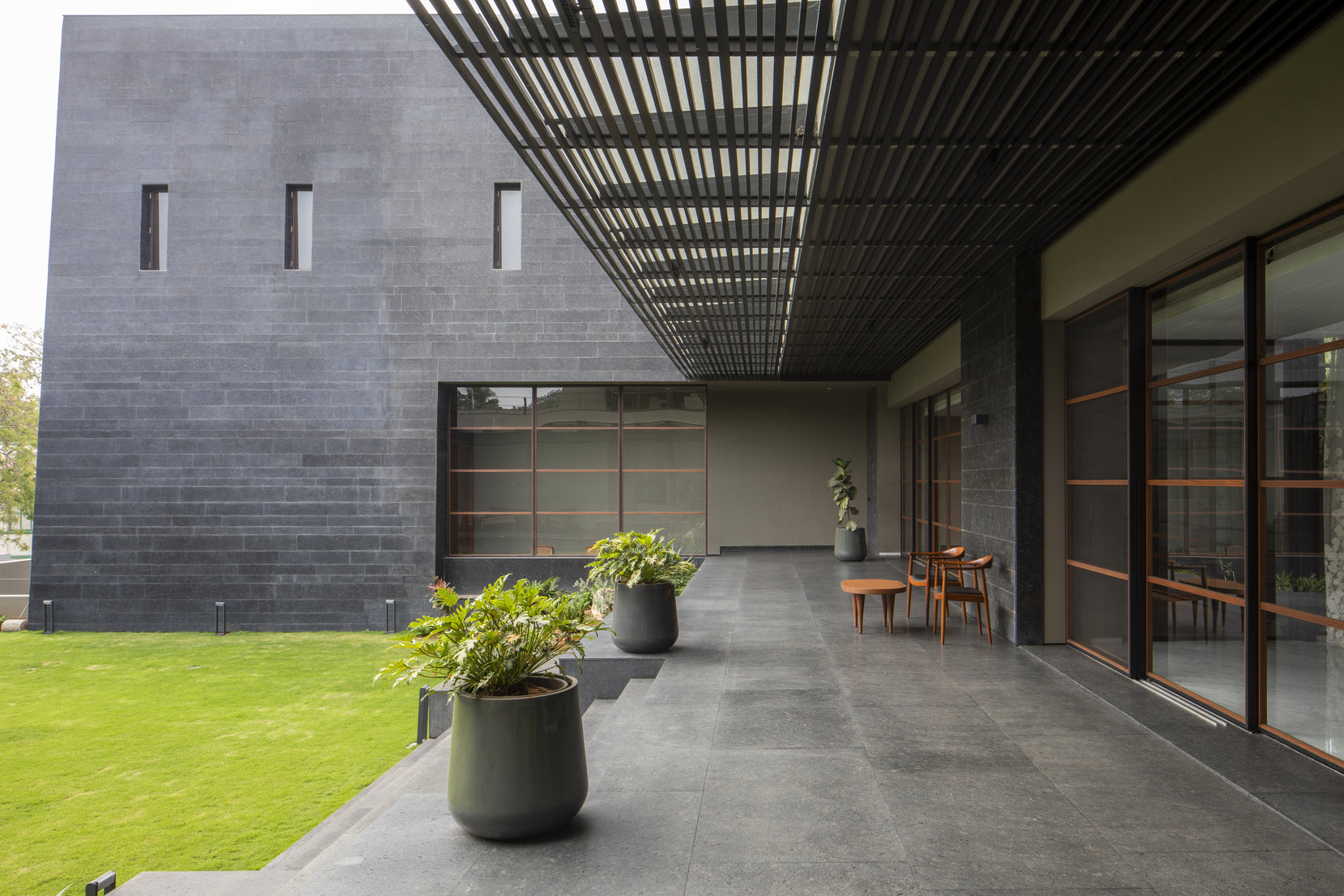 Verandah under a black slatted pergola, potted ferns lining the edge of the lawn