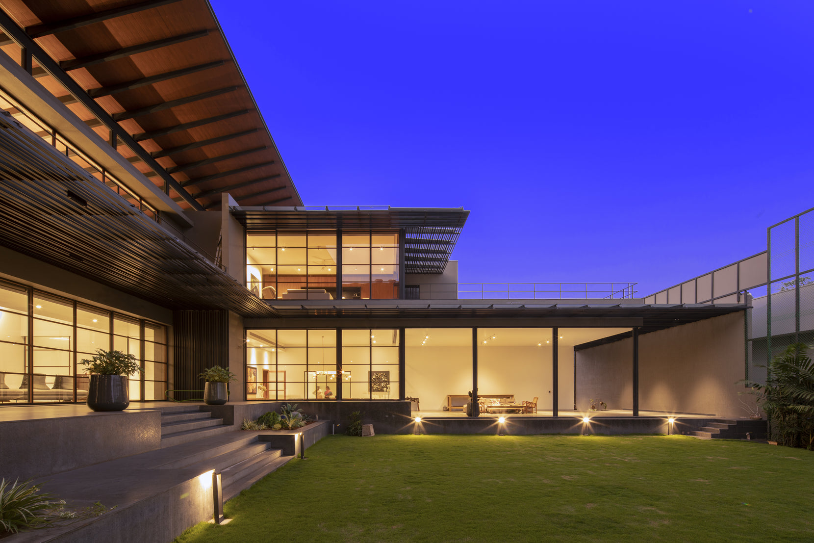 Courtyard elevation lit against a deep blue evening sky, living room open onto the lawn