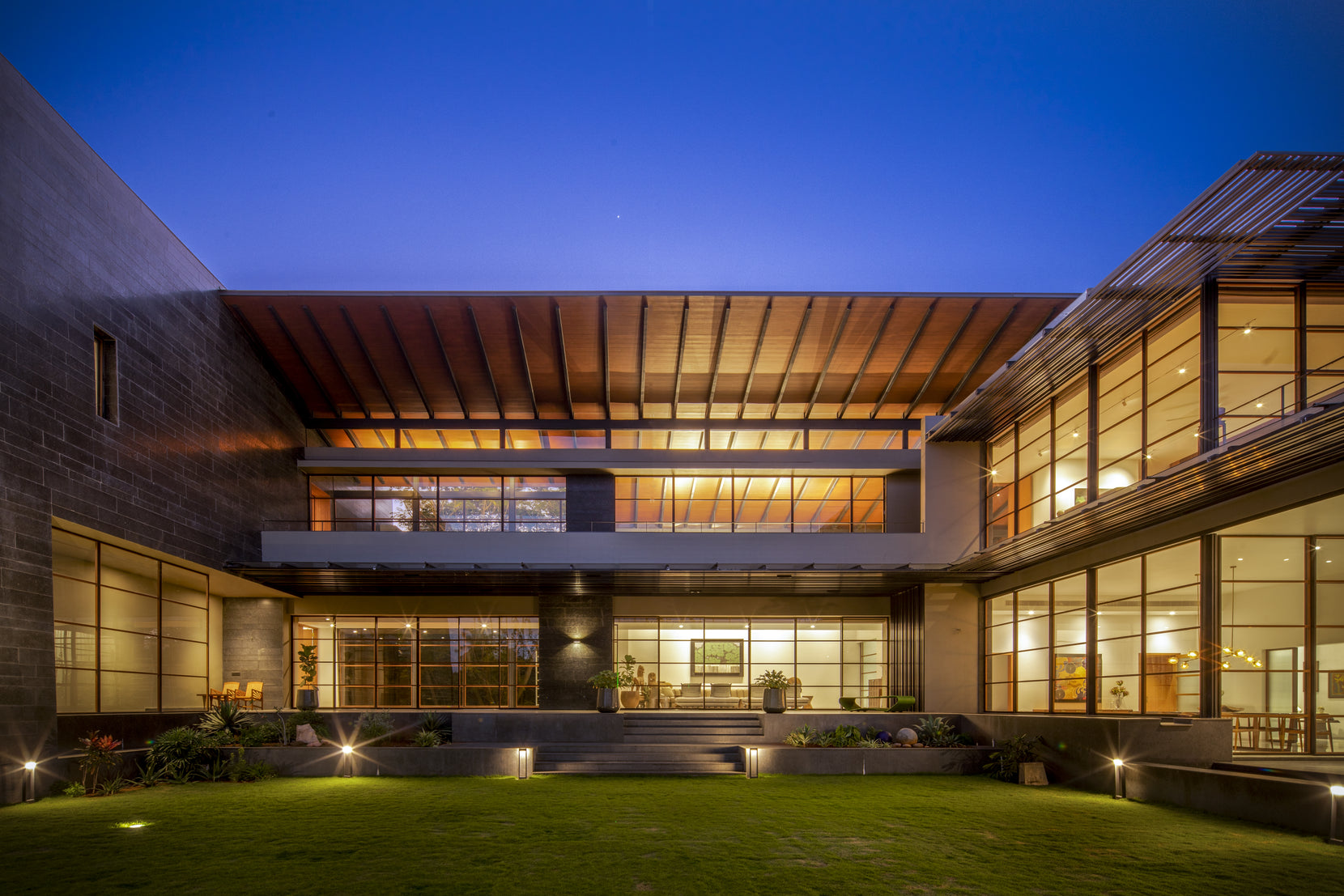 Black Bastian at dusk, the lit living pavilion held between two dark granite bastions