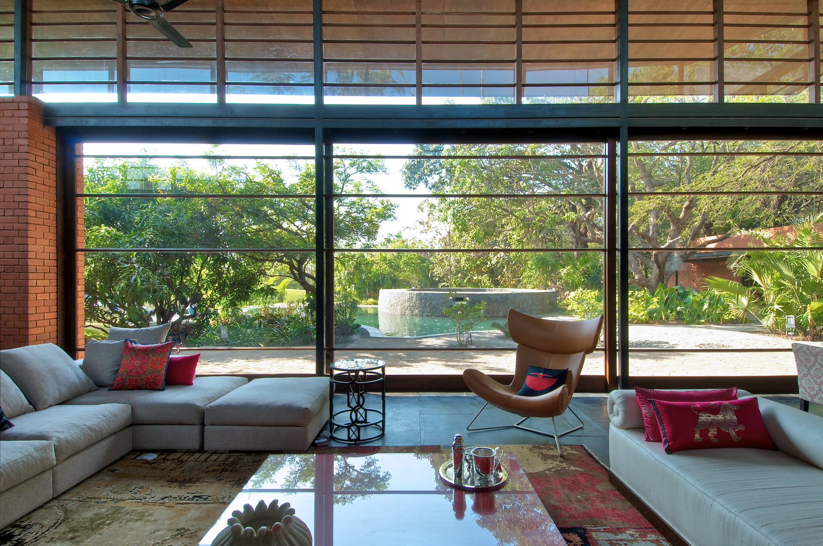Living room behind full-height glazing, cane blinds above and the pool visible in the garden