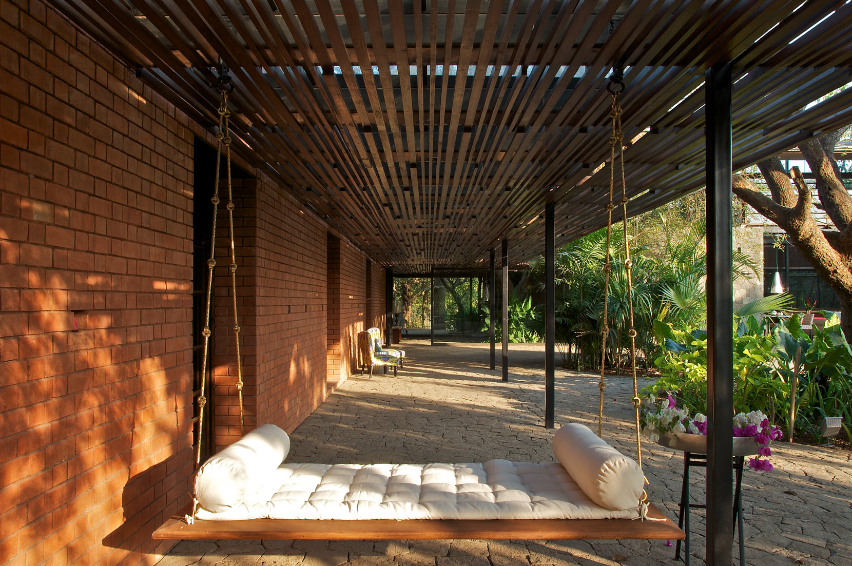 Rope-hung swing bed with a white mattress in the brick-walled verandah