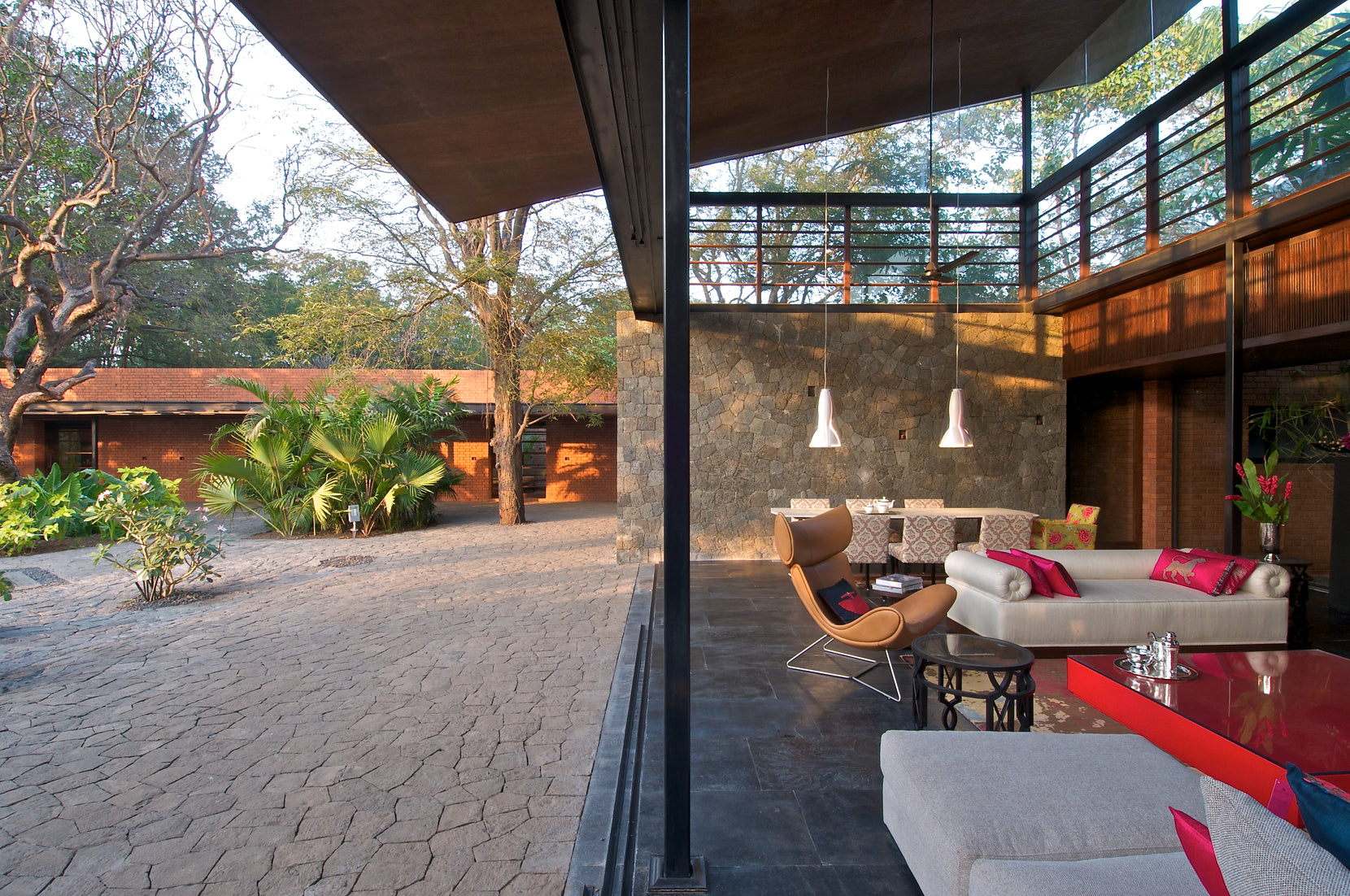 Open-sided living room with a stone wall and double-height gallery, courtyard paving beyond