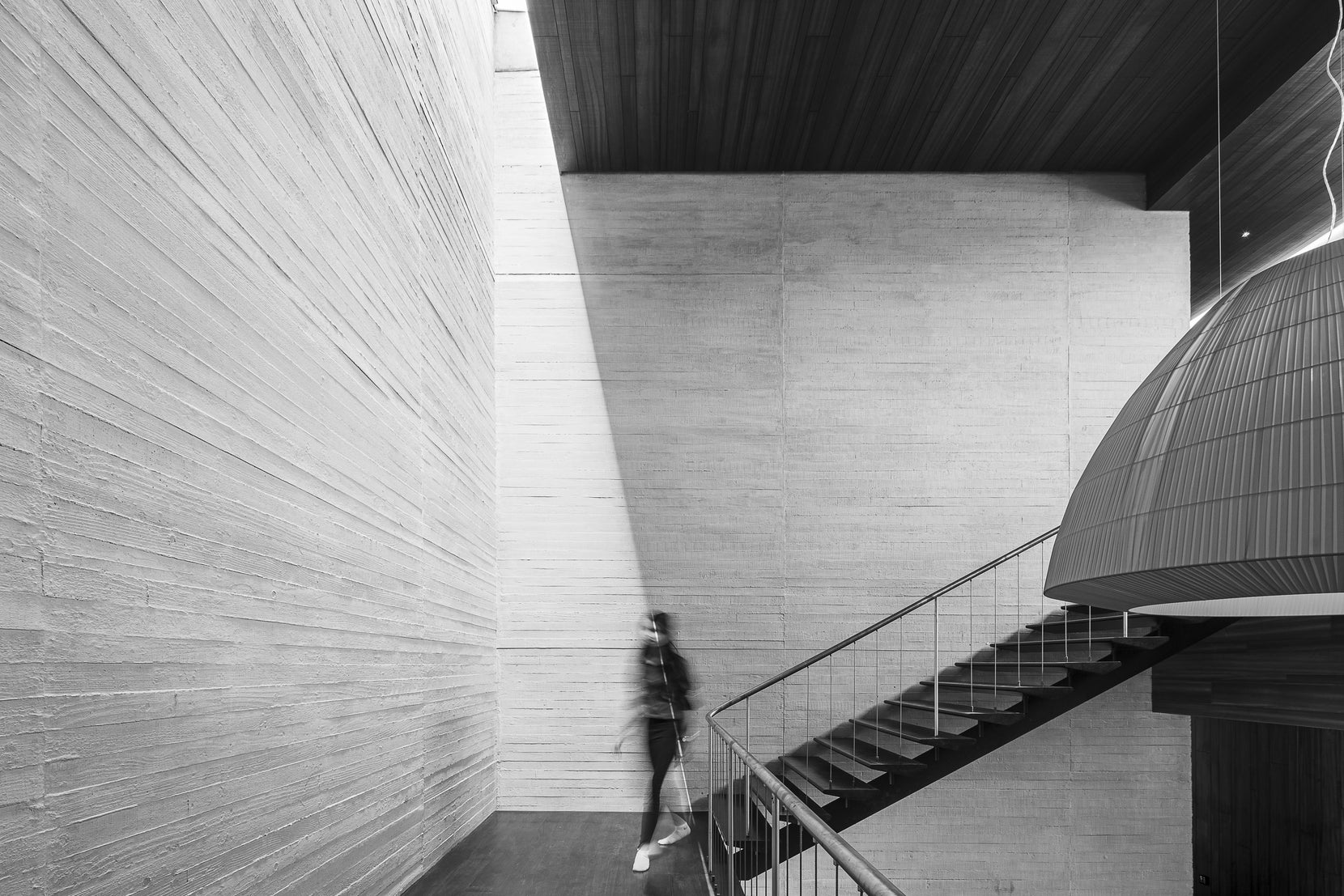 Figure descending the steel stair between shuttered concrete walls, in black and white