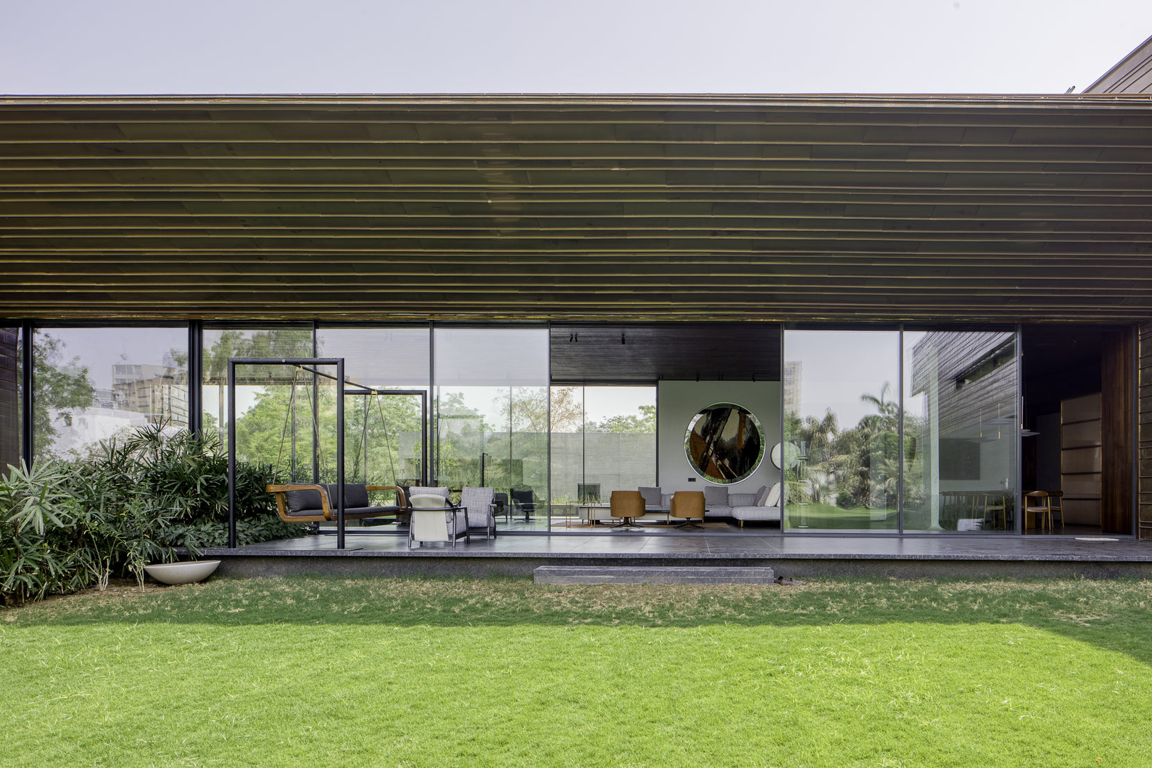 Living room opening fully to the lawn beneath a deep timber-lined soffit