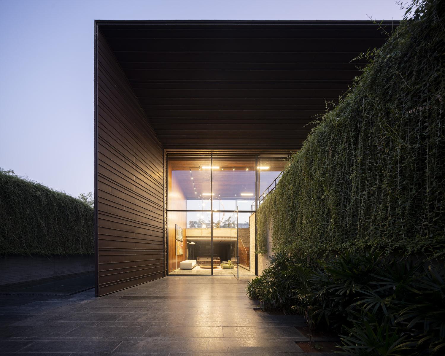 Copper House entrance court at dusk, ribbed copper wall facing a curtain of creeper
