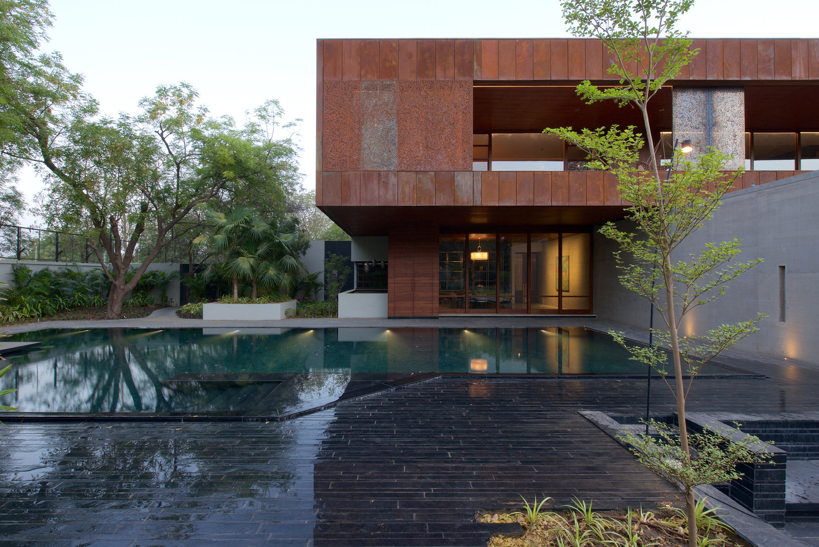 Corten box over the pool deck, with a young tree and dark stone paving in the foreground