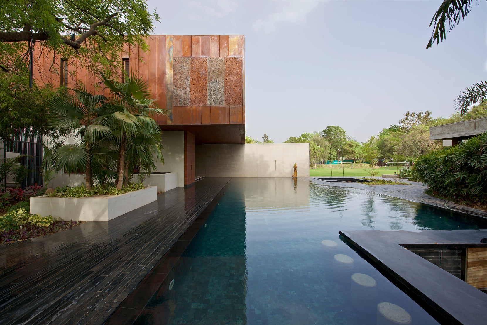 Corten volume of Diya House reflected in the long pool, the lawn and trees opening beyond