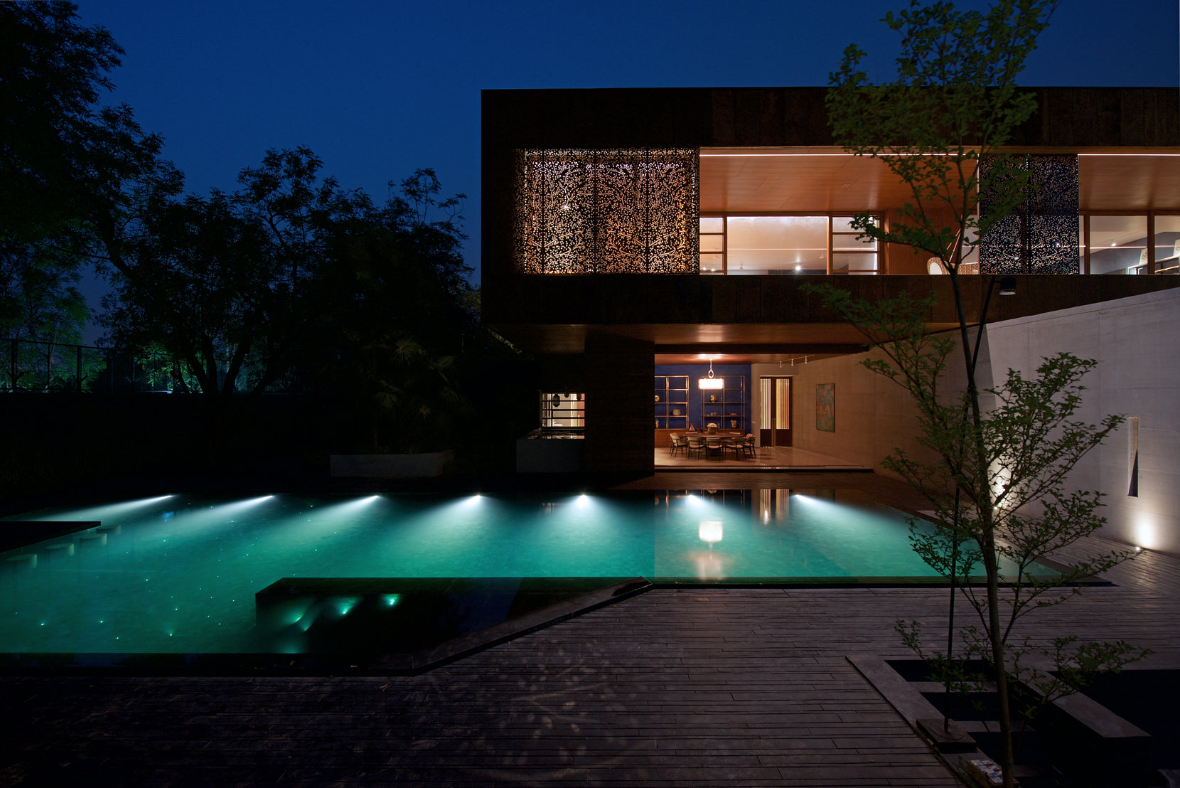 House at night with the pool floodlit and a perforated screen glowing on the upper floor