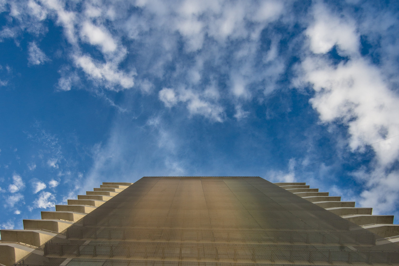Looking straight up the mesh-clad edge, terrace slabs stepping out either side against blue sky