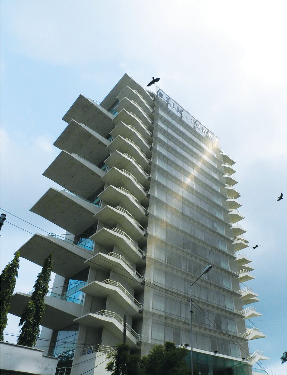 Exim Tower from street level, sunlight striking the stainless mesh screen as birds pass