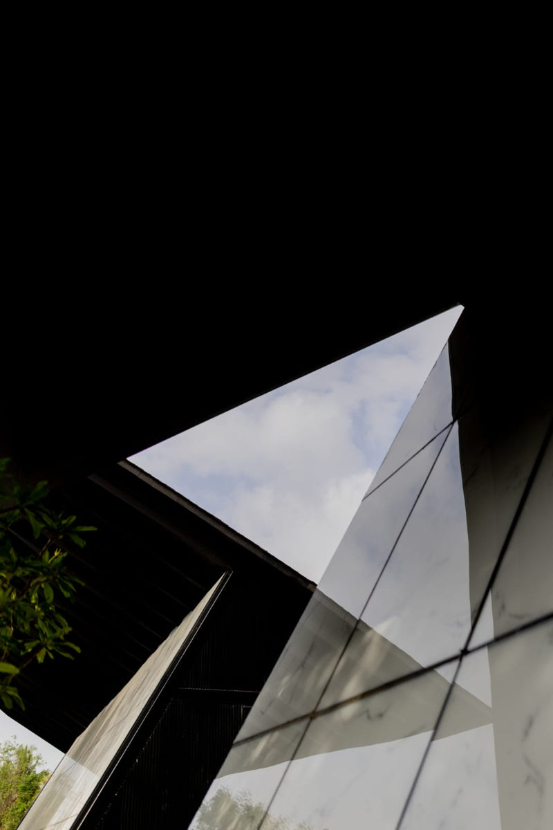 Marbled glass wall tilting up to a sharp roof edge that mirrors the clouded sky