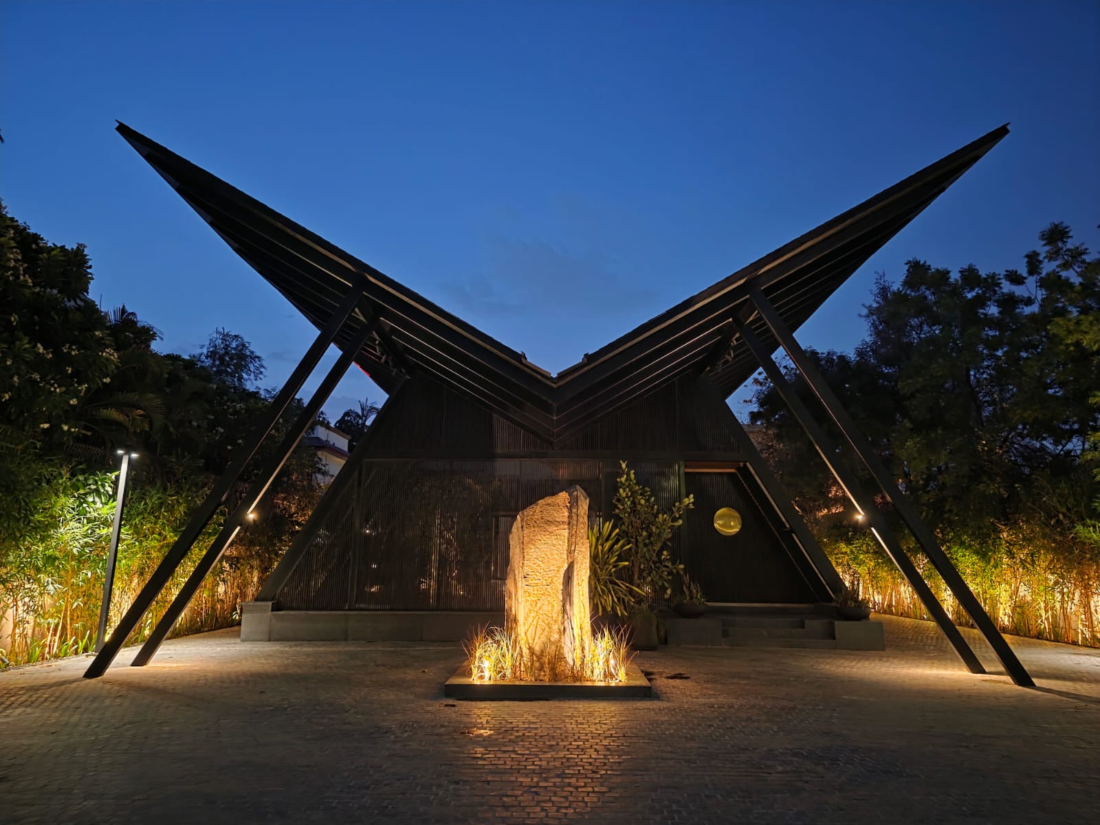 Symmetrical wings of the roof at night, a lit boulder standing in the forecourt