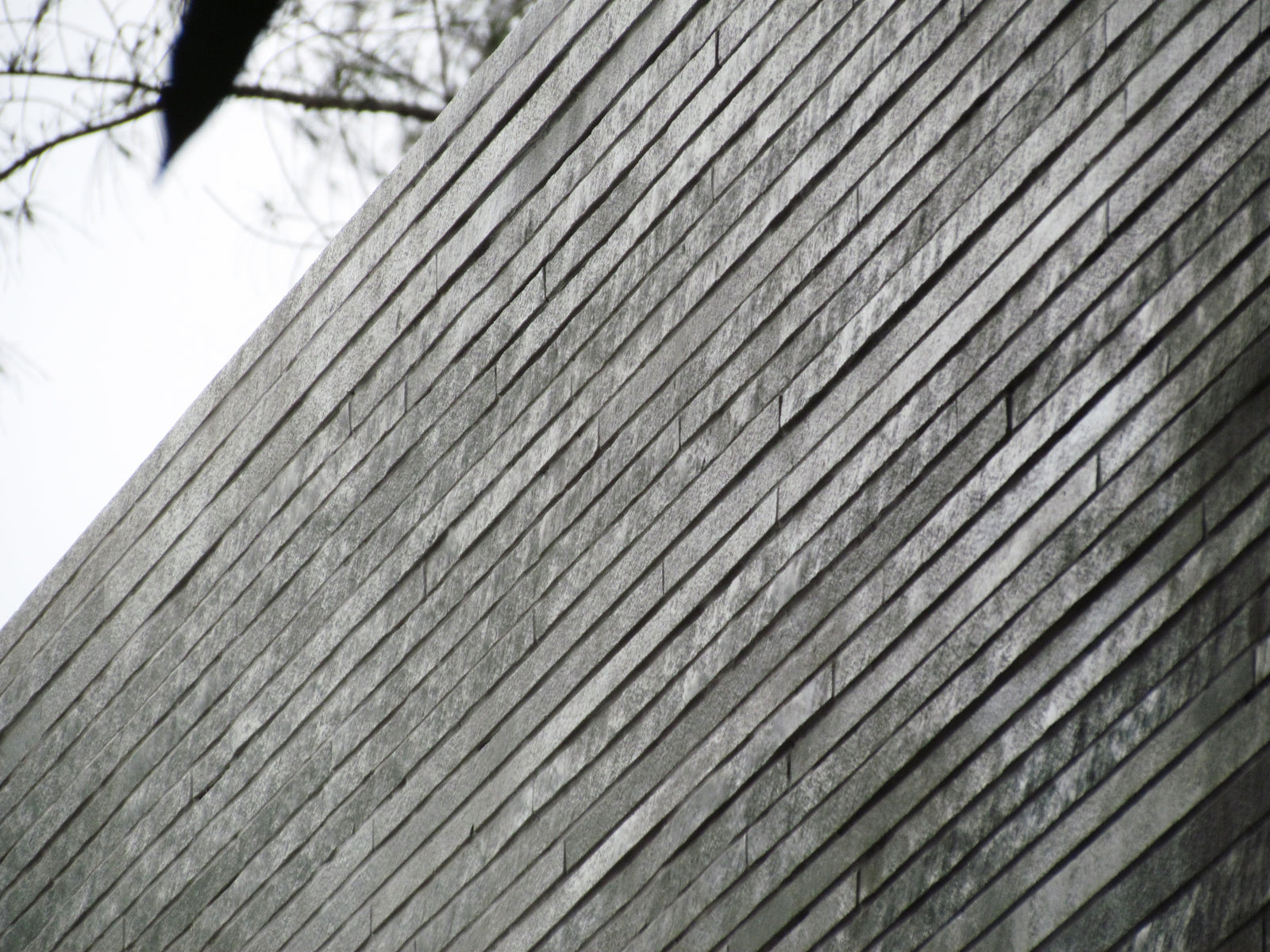 Coursed grey stone wall raking up against an overcast sky, seen from below