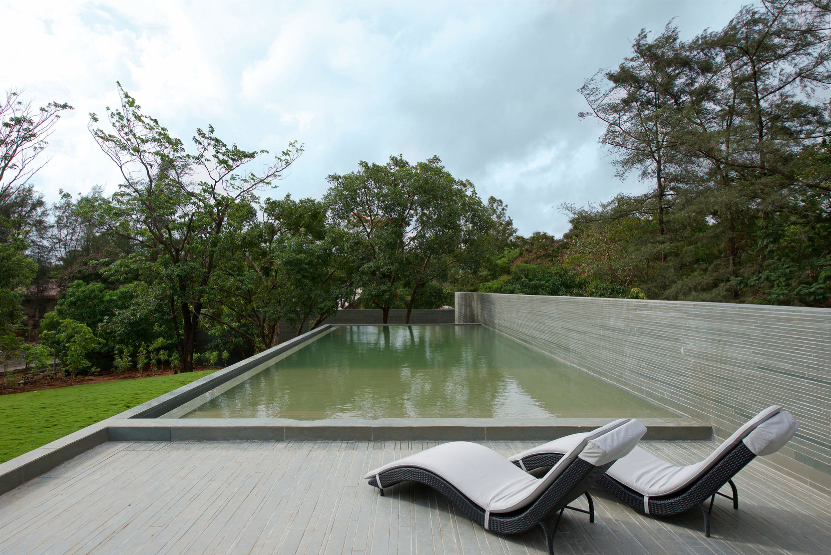 Lap pool edged by a coursed stone wall, two loungers on the deck under monsoon cloud