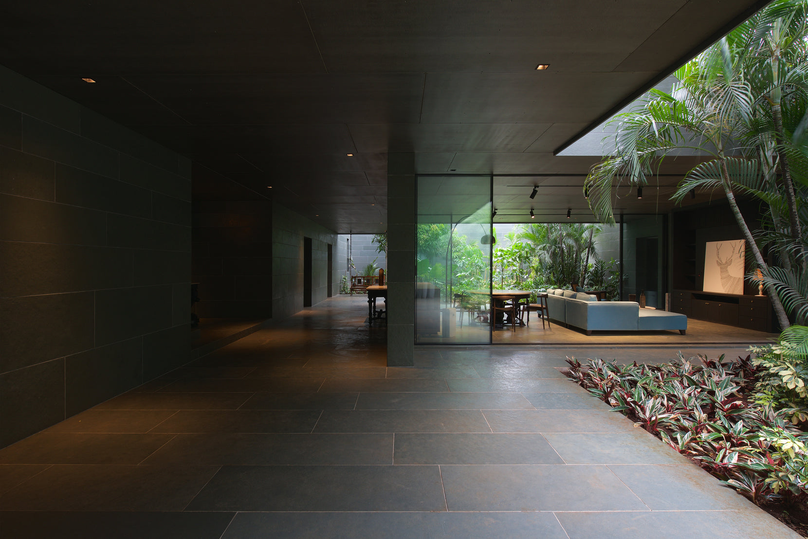 Dark stone-lined passage at Gomati opening to a glazed living room and planted courtyard
