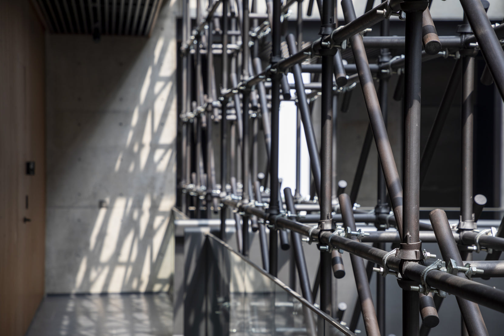 Clamped steel tube screen against raw concrete and timber, seen in close detail