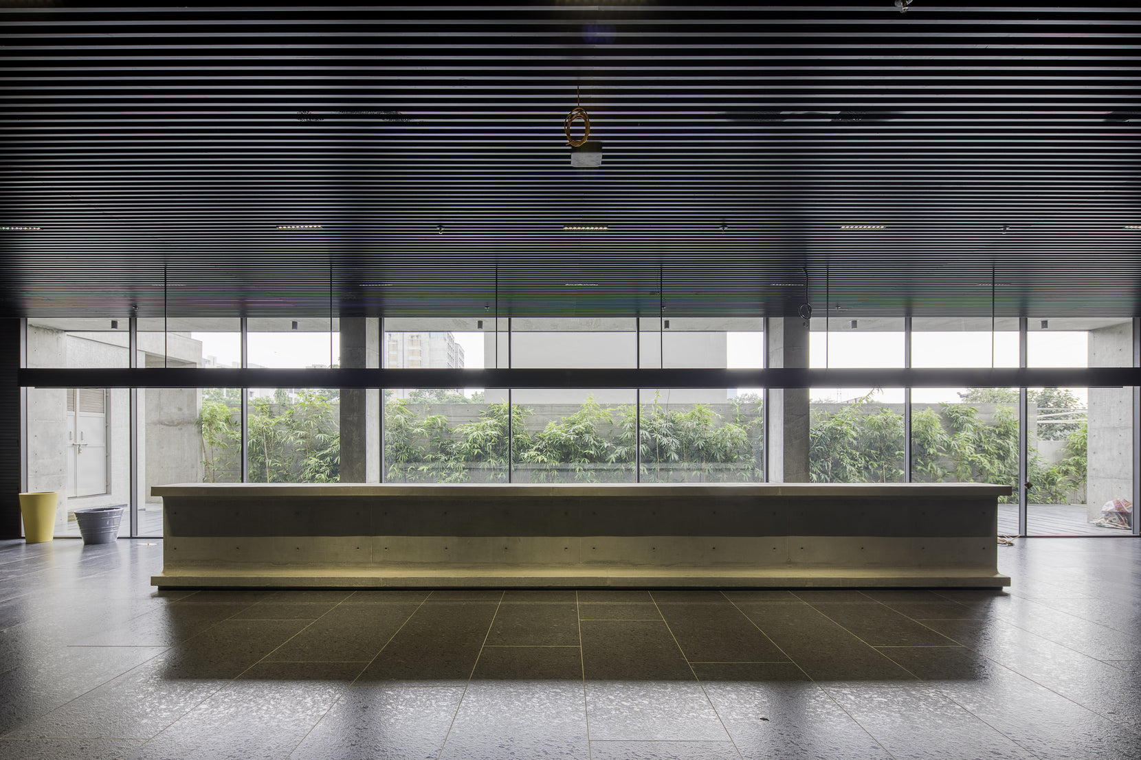 Cast concrete I-girder reception desk set against full-height glazing onto greenery