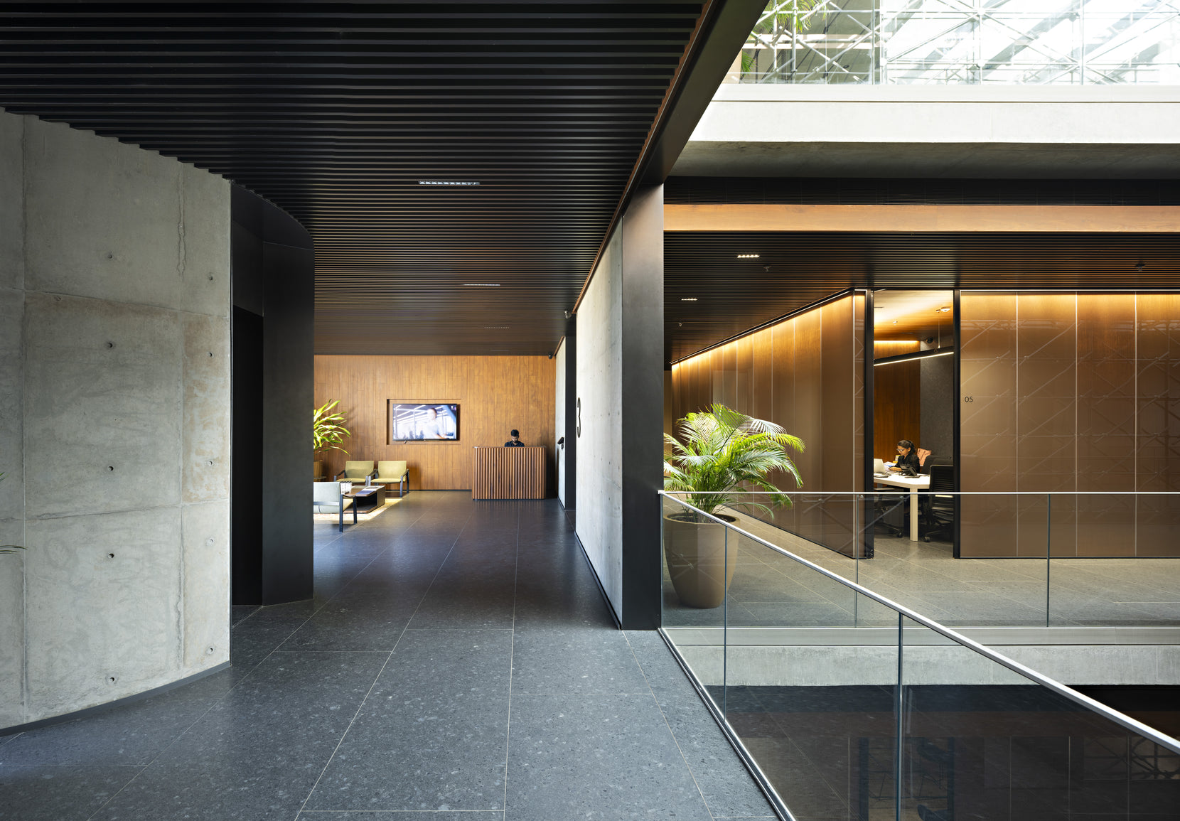 Lobby with a curved concrete wall and glazed meeting rooms panelled in timber beyond