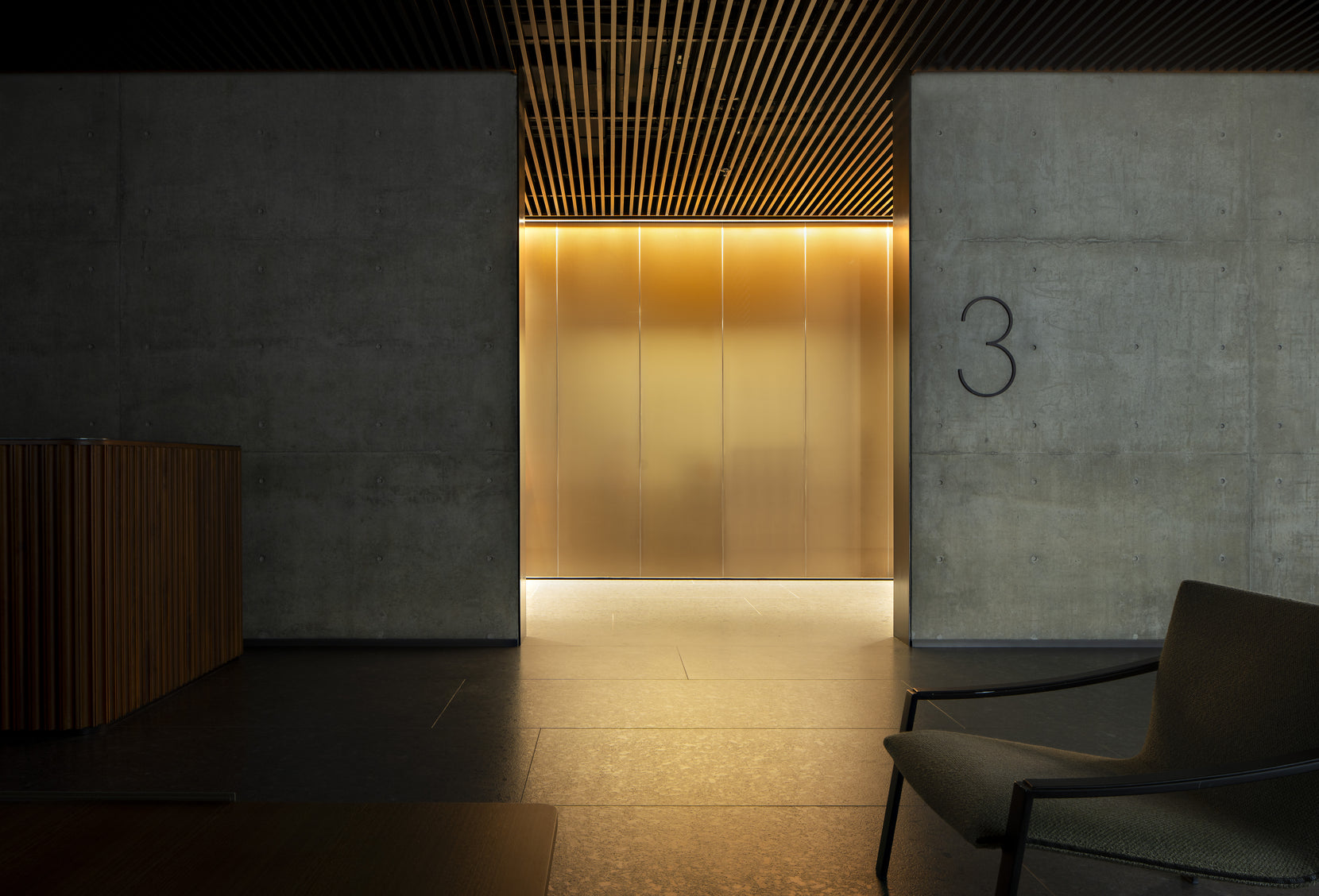 Lift lobby lined in brushed brass, the level number cut into the concrete wall