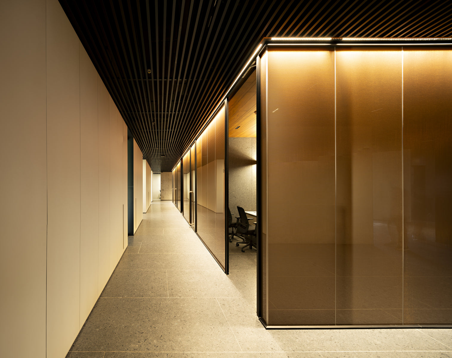 Office corridor beside a brass-clad meeting room, slatted ceiling running its length