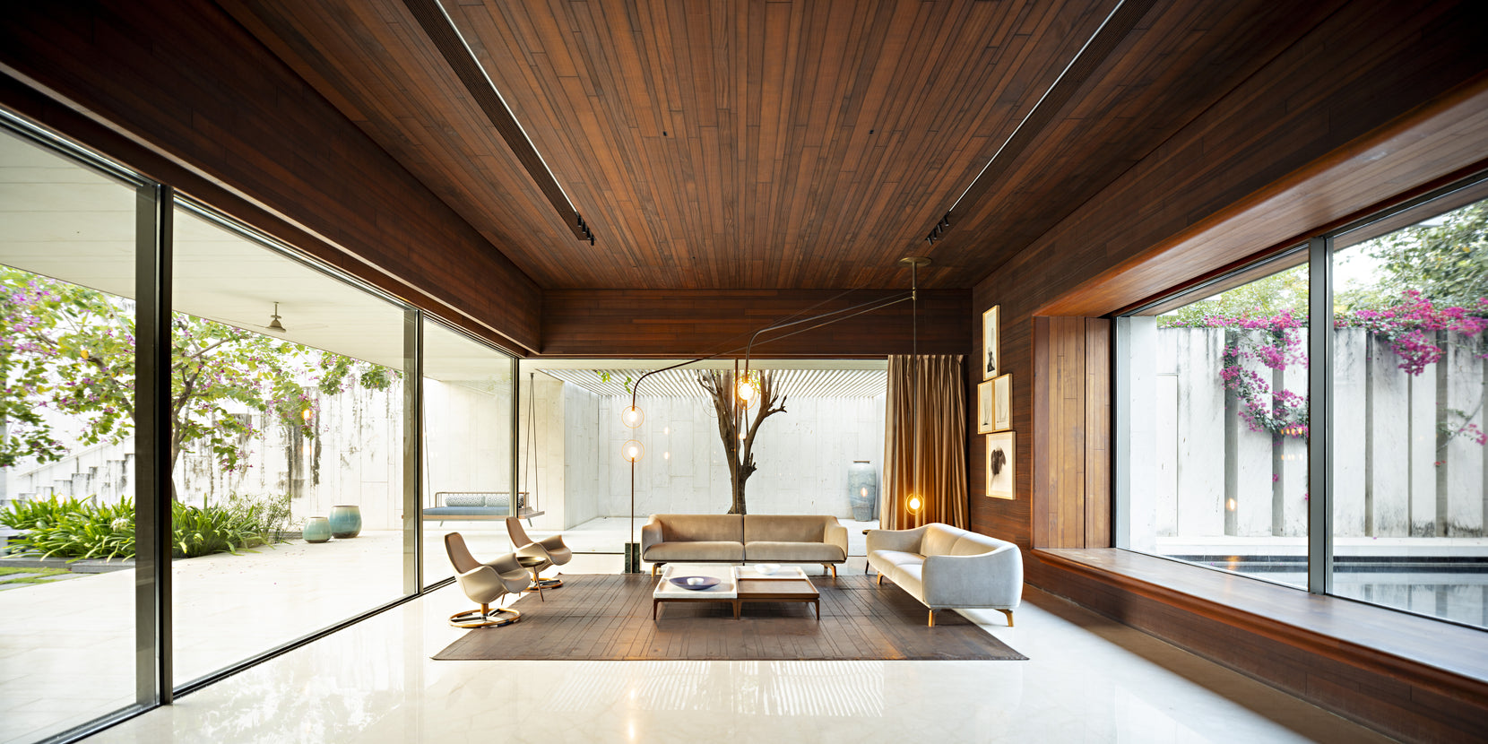 Living room under a dark timber ceiling, glazed to a courtyard tree on one side and water beyond