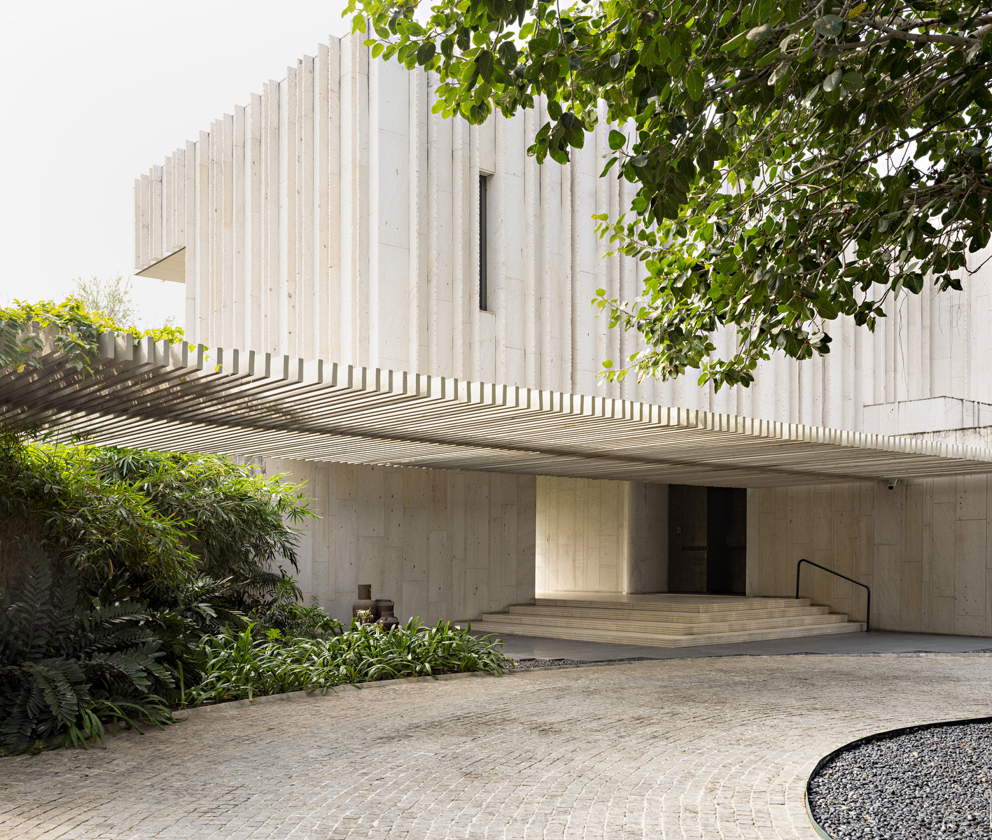 Entrance court at House of Secret Gardens, timber louvres shading steps below a fluted stone block