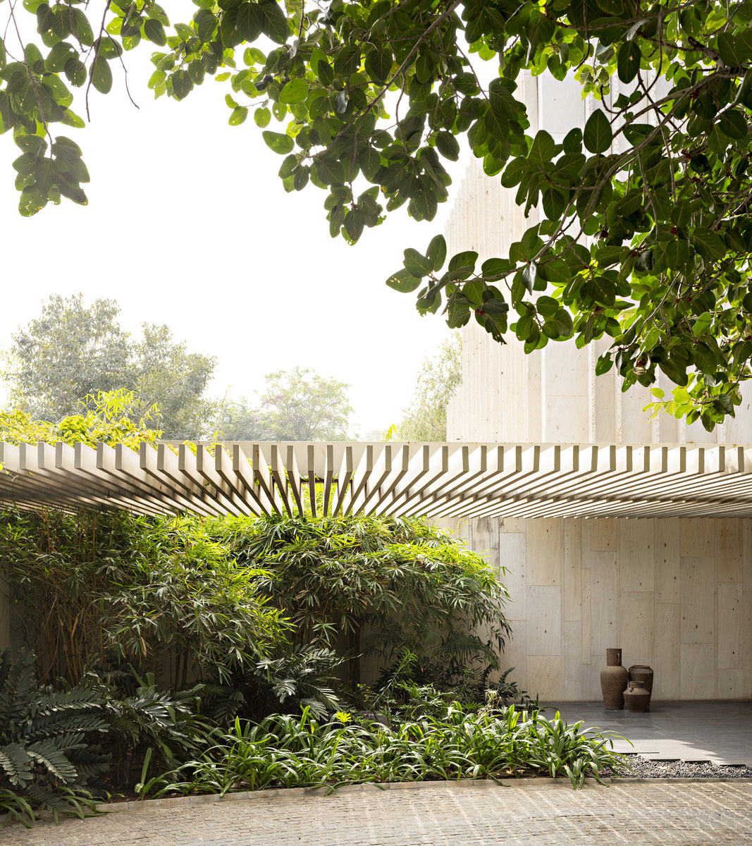 Ribbed pergola reaching over a dense planted court, two urns standing against the stone wall