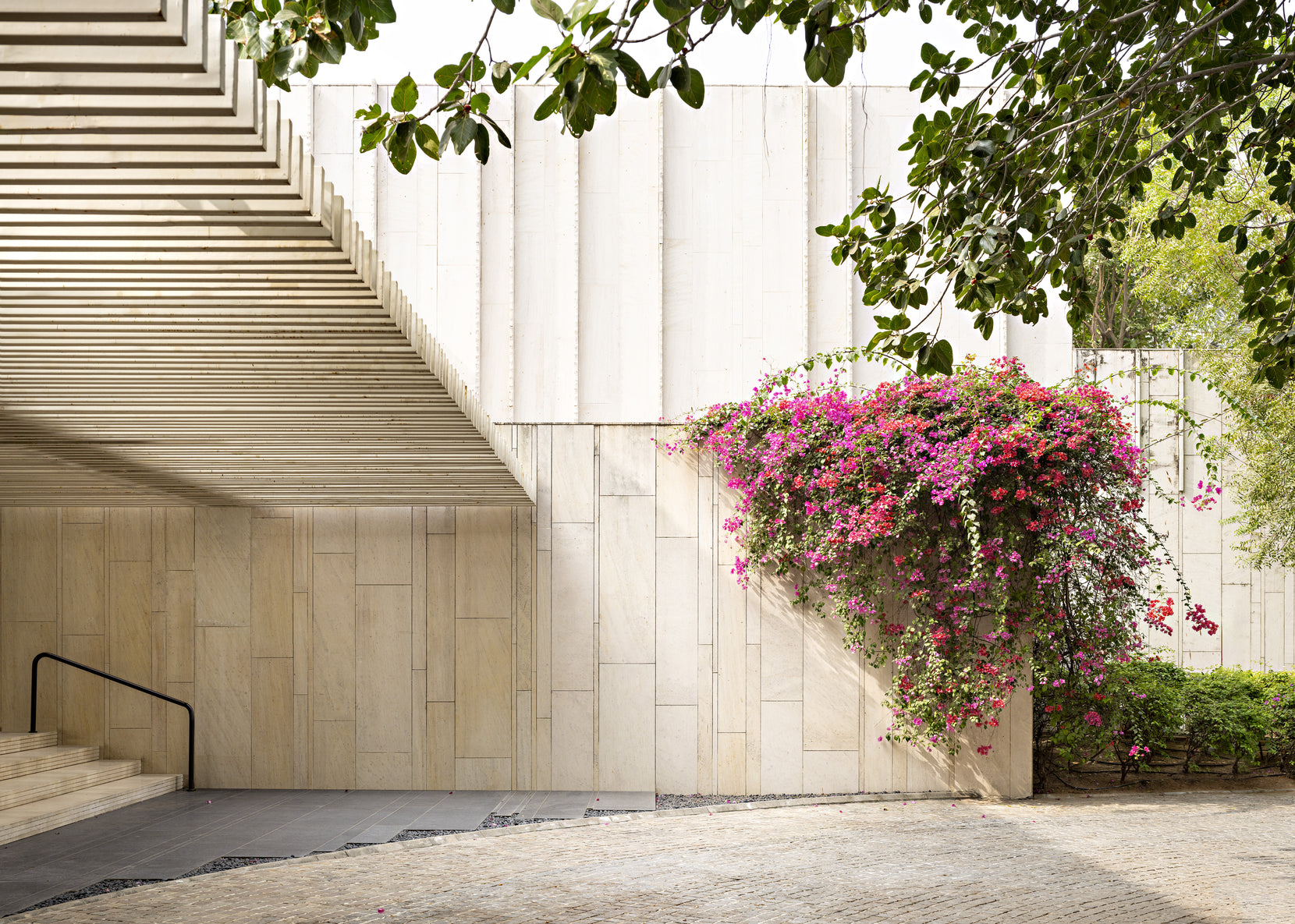 Underside of the external stair cutting across a sandstone wall, bougainvillea cascading beside it