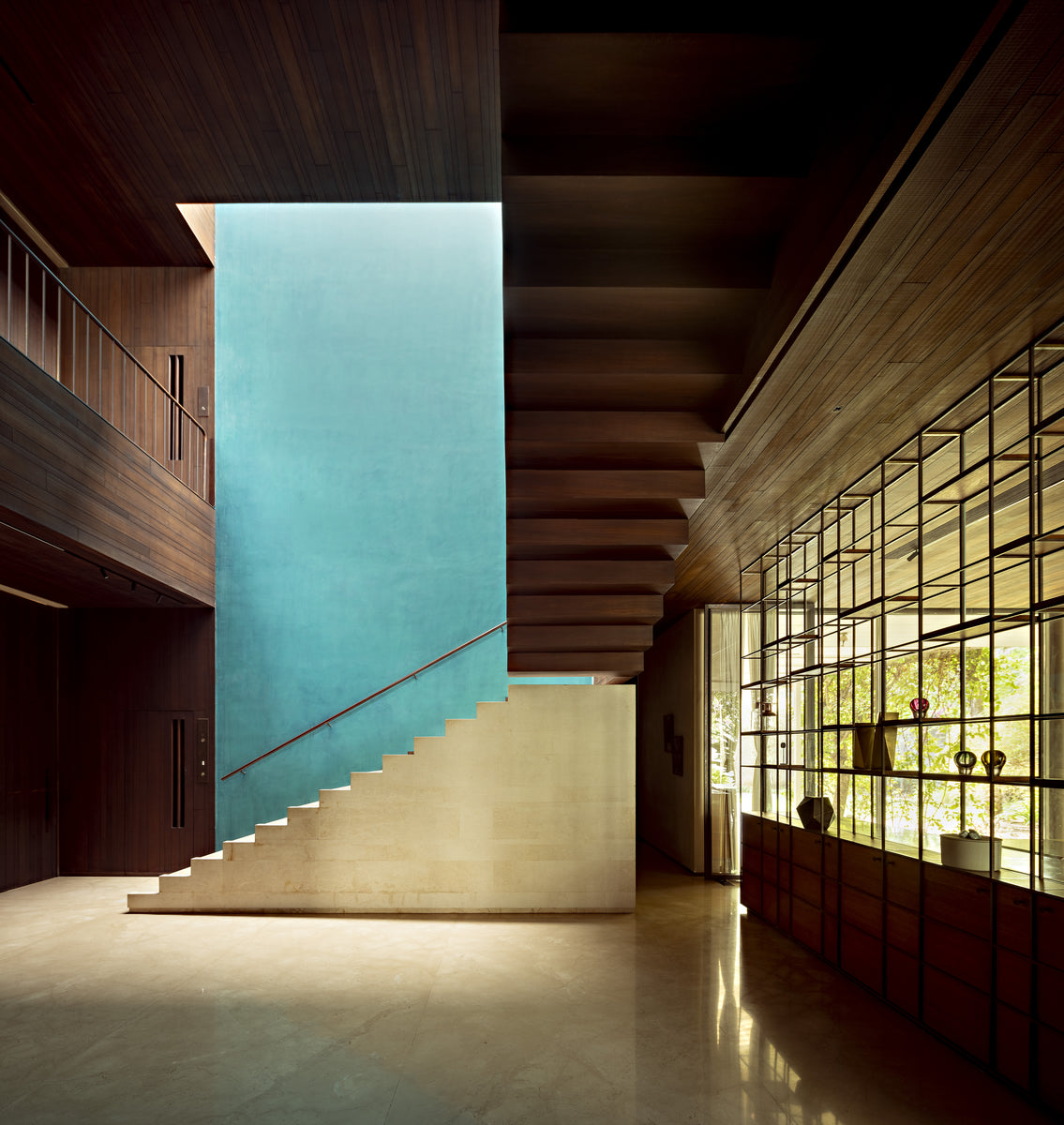 Cantilevered stair against a turquoise wall in the double-height hall, brass shelving alongside