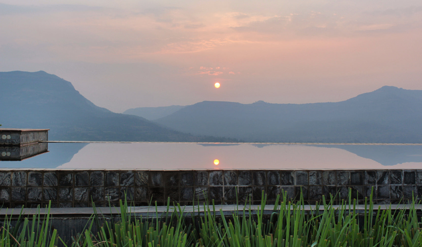 Sun setting over Pawna Lake above the pool, gabion stonework and grasses in the foreground