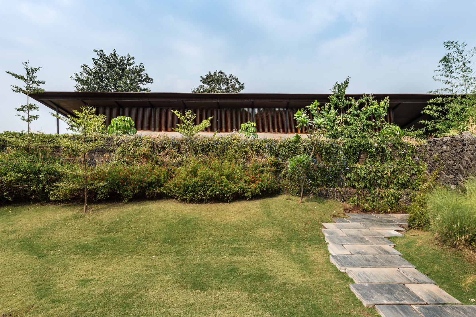 The house viewed across the lawn, its slim roof sitting above a stone gabion retaining wall