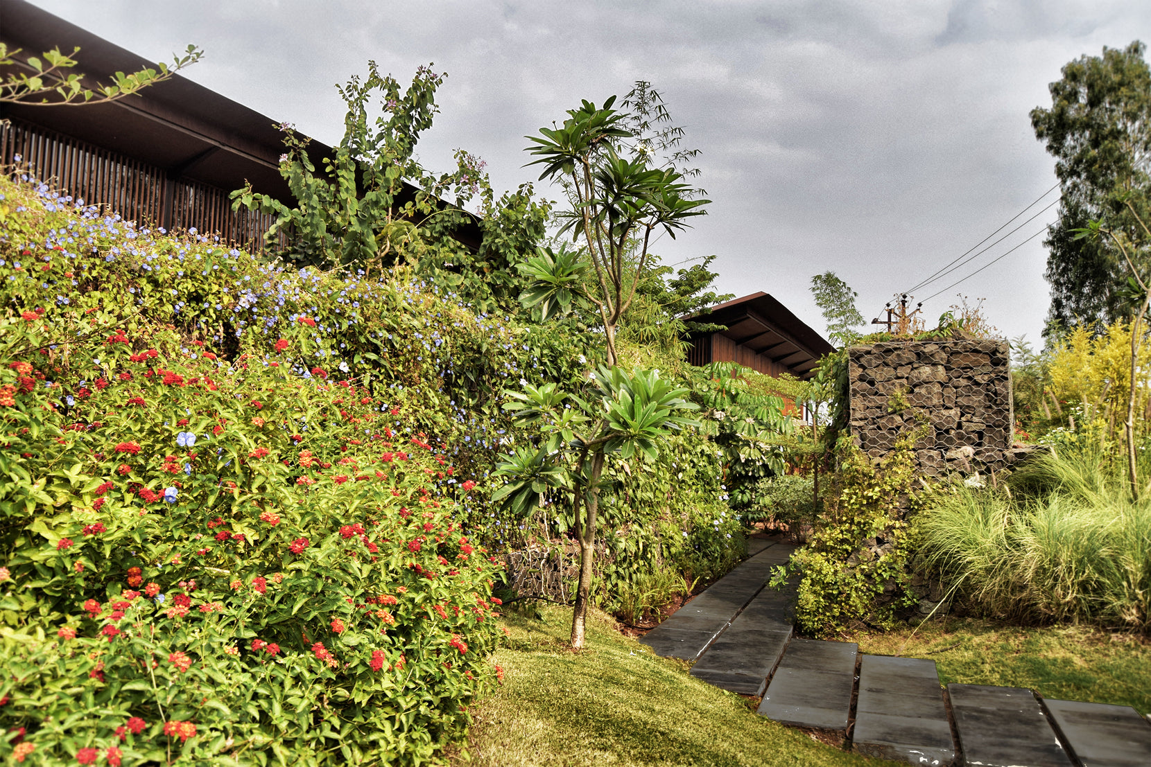 Flowering shrubs on the slope with the roof edge and a stacked stone gabion pier behind