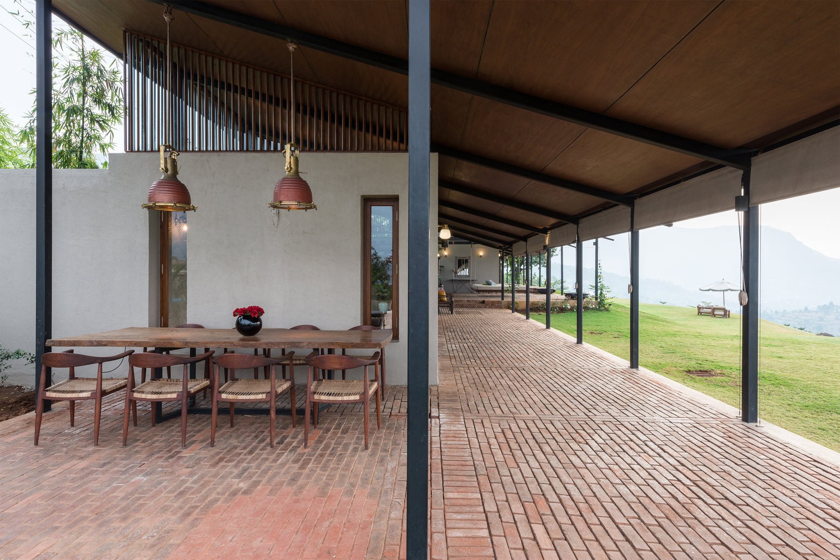 Dining table and copper pendants under the verandah, brick paving continuing past the columns