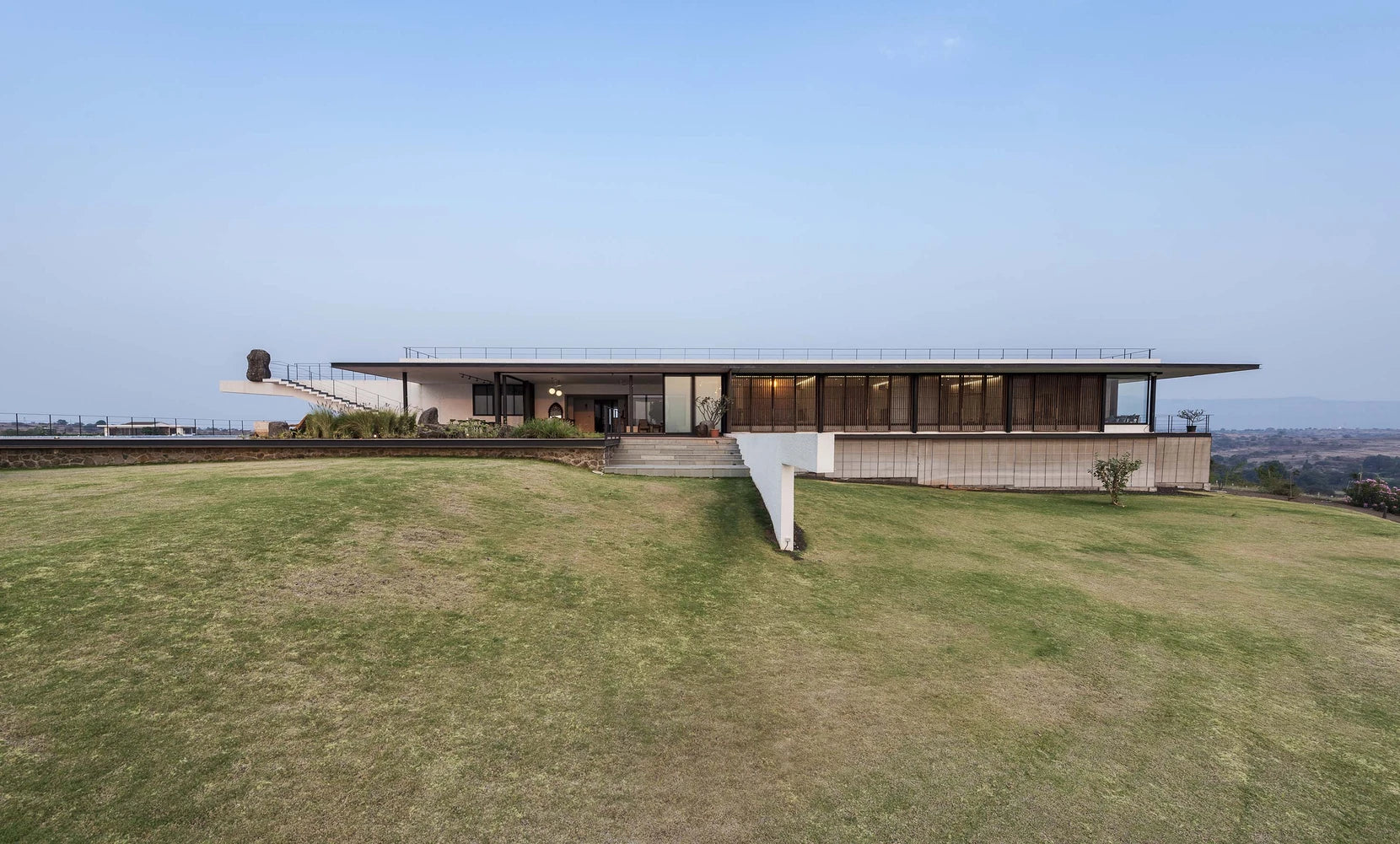 Long horizontal roof of the house held above the crest of the lawn, hills in the distance