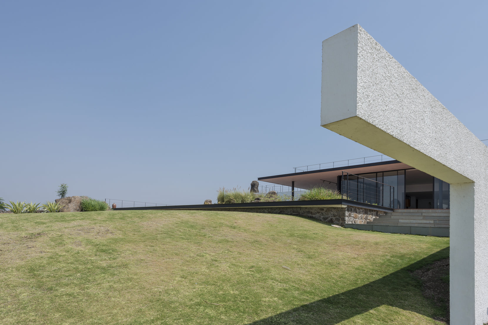 White cantilever cutting across the sky above the mounded lawn, the house set low behind