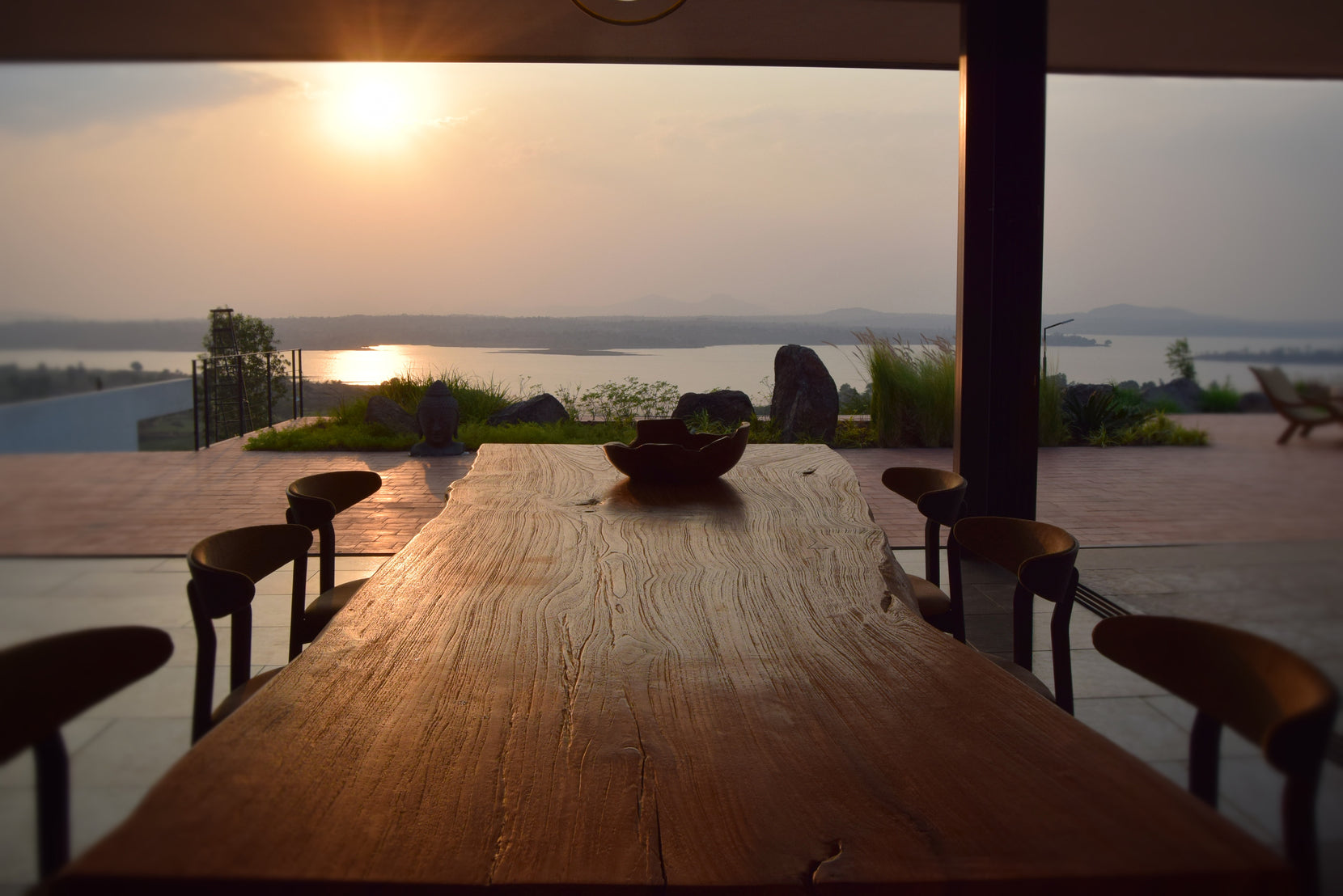 Live-edge timber dining table facing the reservoir as the sun sets