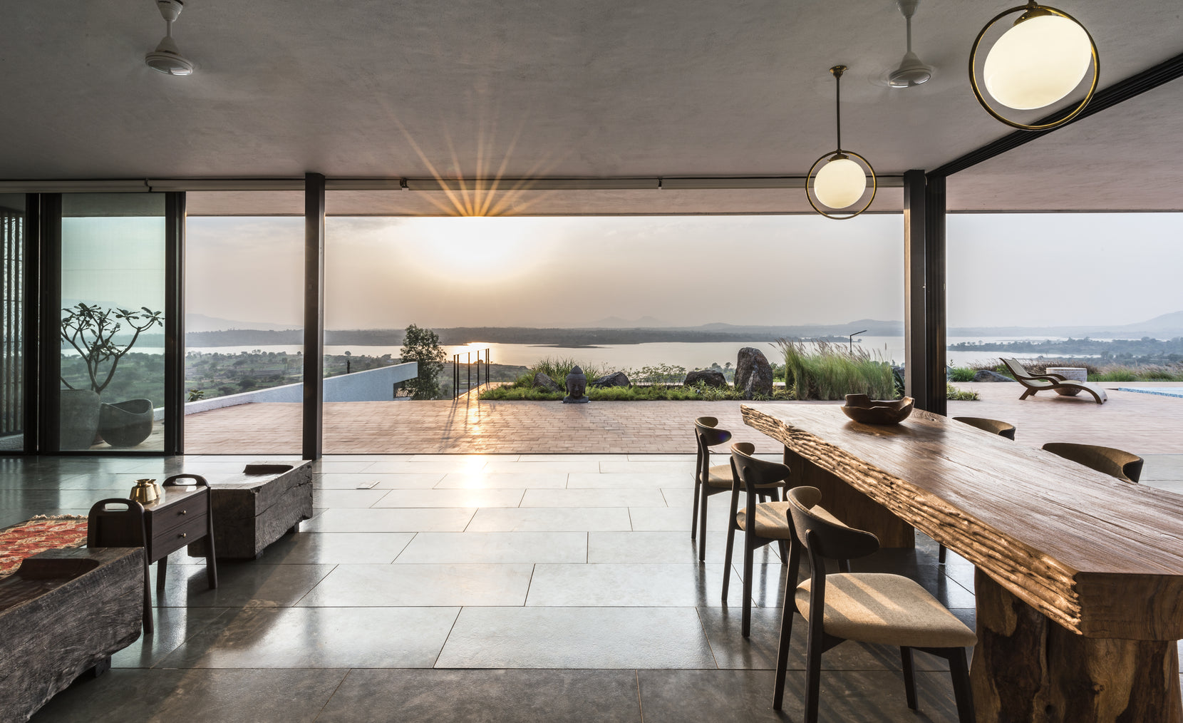 Living and dining spaces opening to the reservoir, the sun setting between sliding glass walls