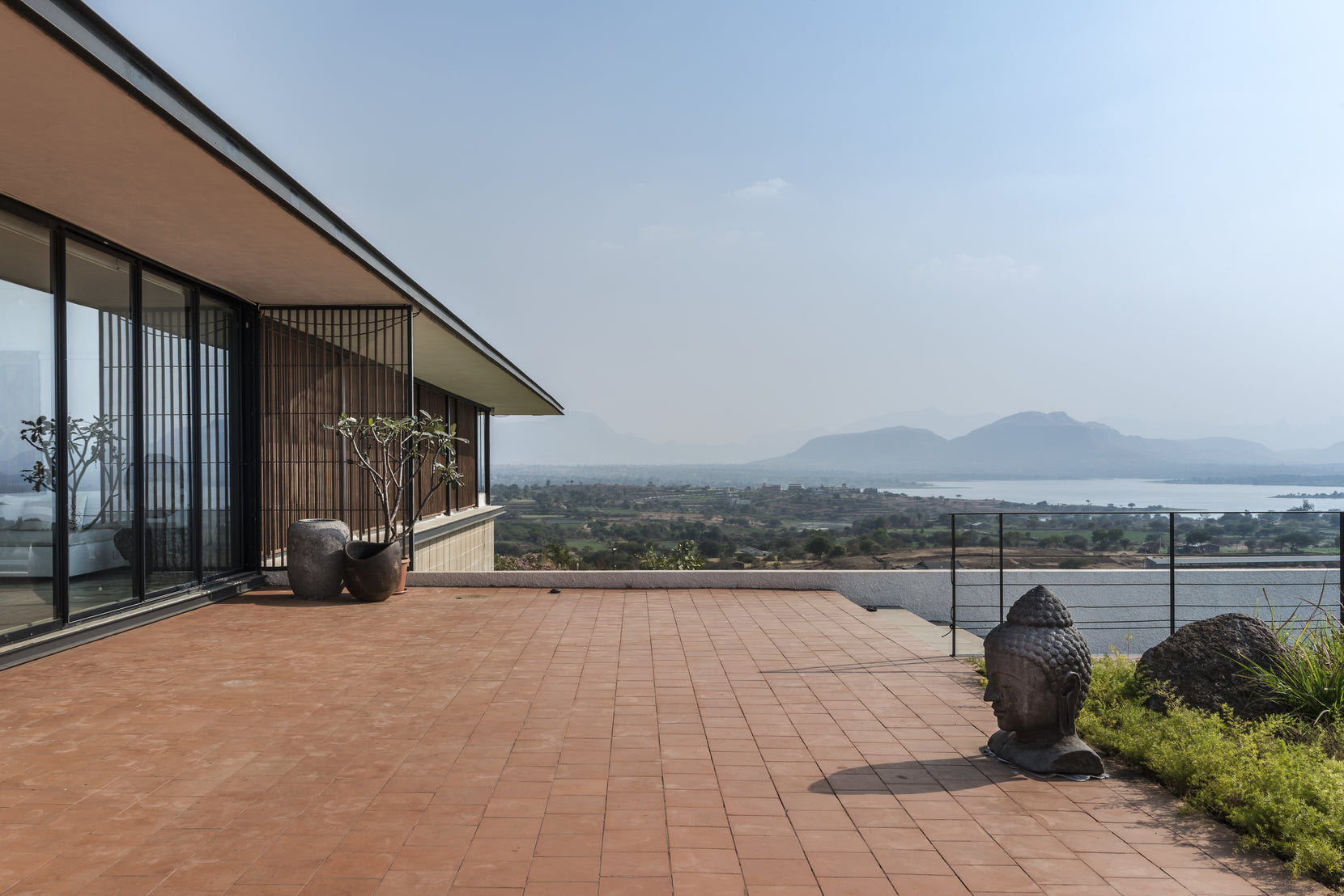Terracotta-tiled terrace with a stone Buddha head, looking over the reservoir to the hills