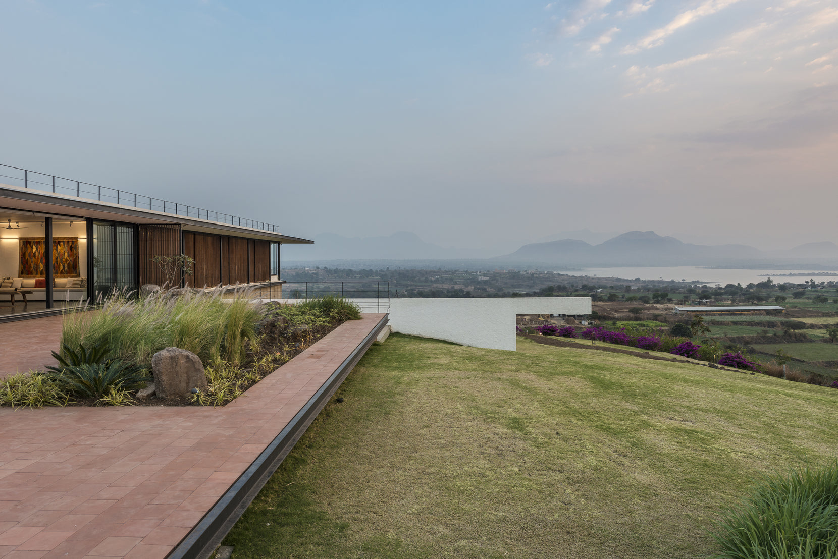 Lit verandah at dusk, the lawn running out to the infinity edge and the valley