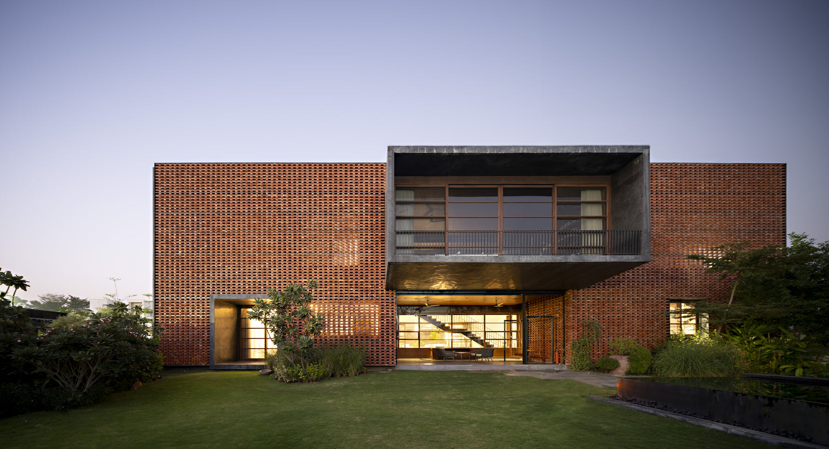 Ishtika's brick jaali elevation at dusk, the projecting balcony framed above a lit ground floor